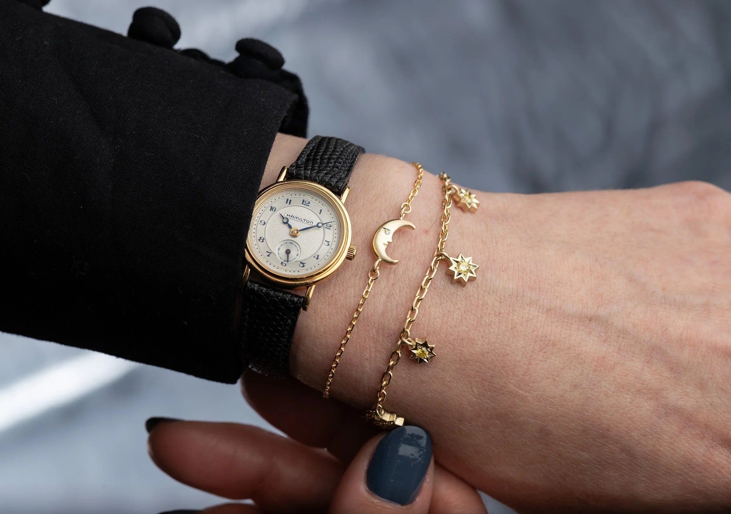 Close-up of wrist with vintage gold watch and delicate gold moon phase and star charm bracelets on natural skin tone