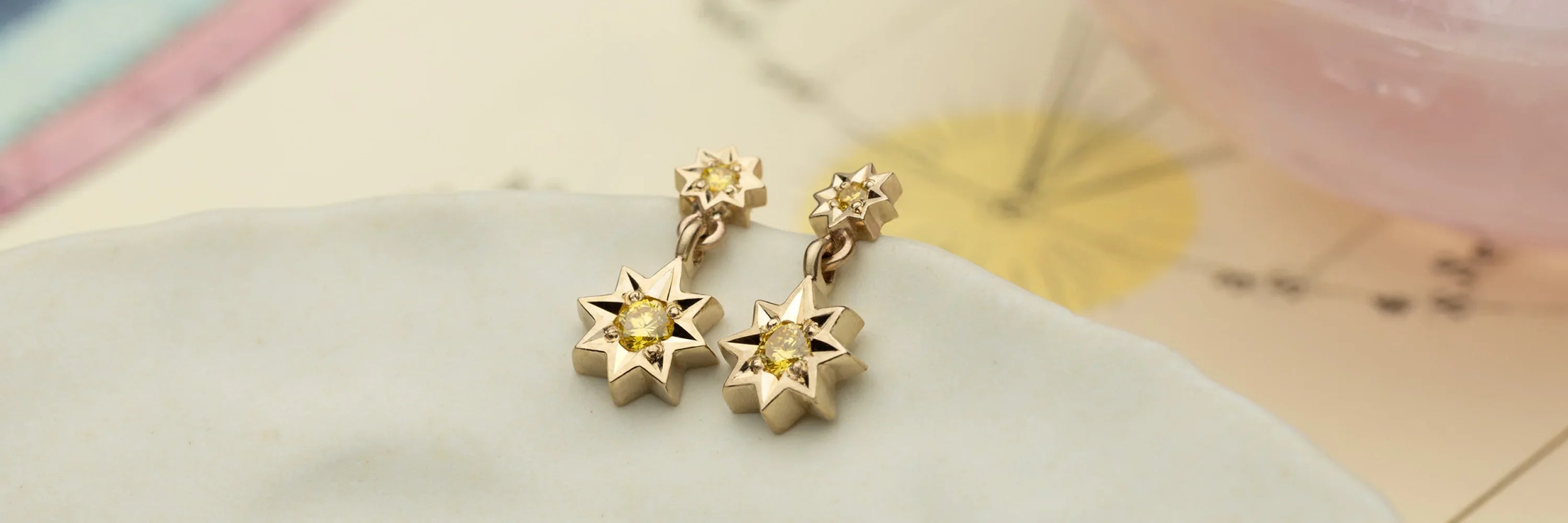 Fairmined gold star-shaped drop earrings with yellow gemstones on soft beige surface