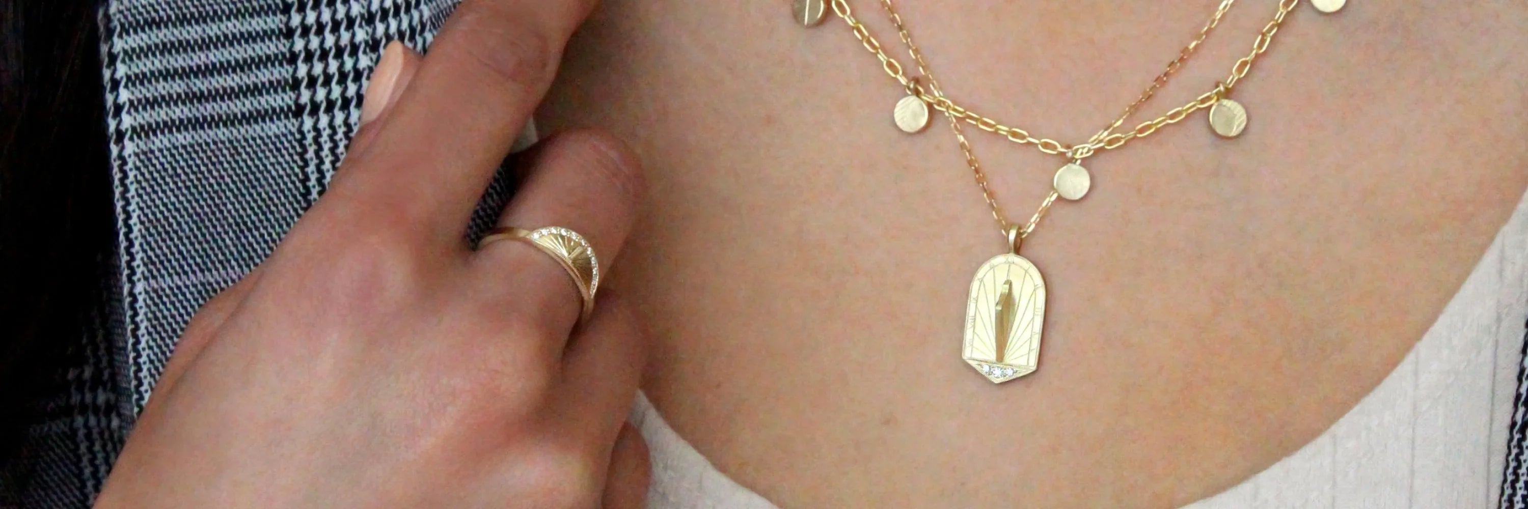 Close-up of hand-fabricated gold sundial pendant and ring with engraved details, warm natural light