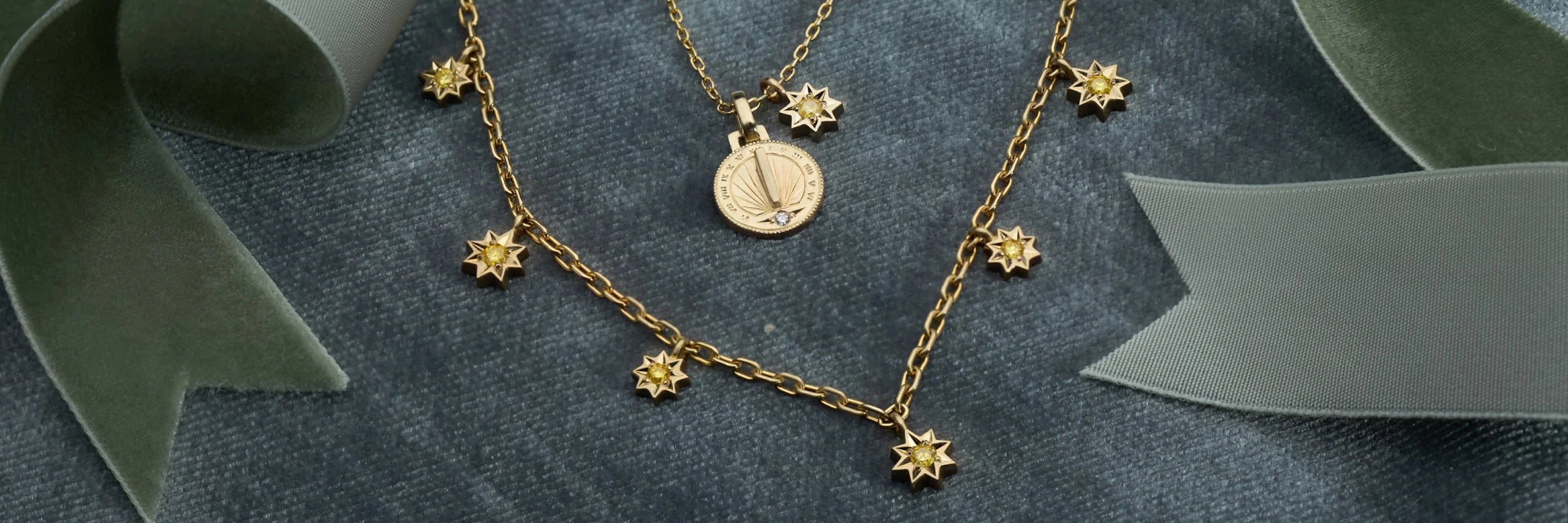 Handcrafted Fairmined gold sundial pendant and star charm necklace on soft velvet background with green ribbon