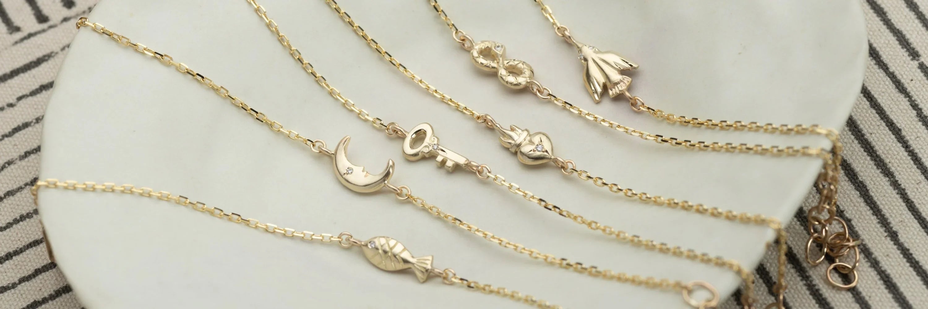 Close-up of delicate gold charm necklaces on white dish, soft natural light and minimalist linen background