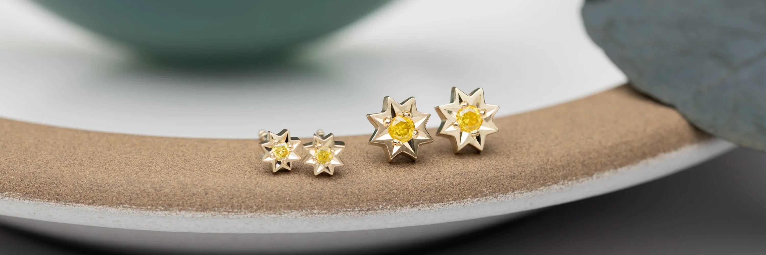 Pair of handcrafted star-shaped gold earrings with yellow gemstone centers on textured ceramic plate