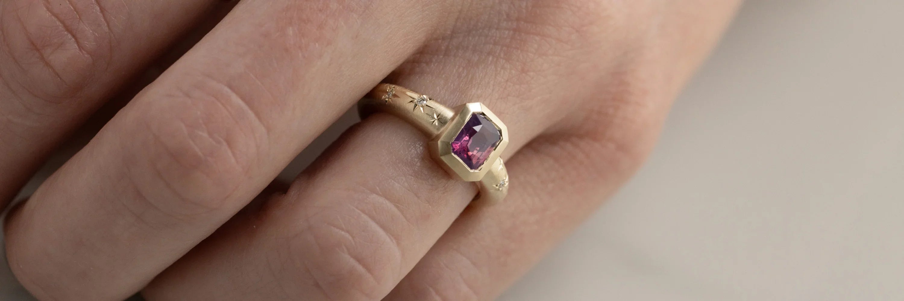 Hand wearing gold ring with pink gemstone and star engravings, soft natural light on neutral background