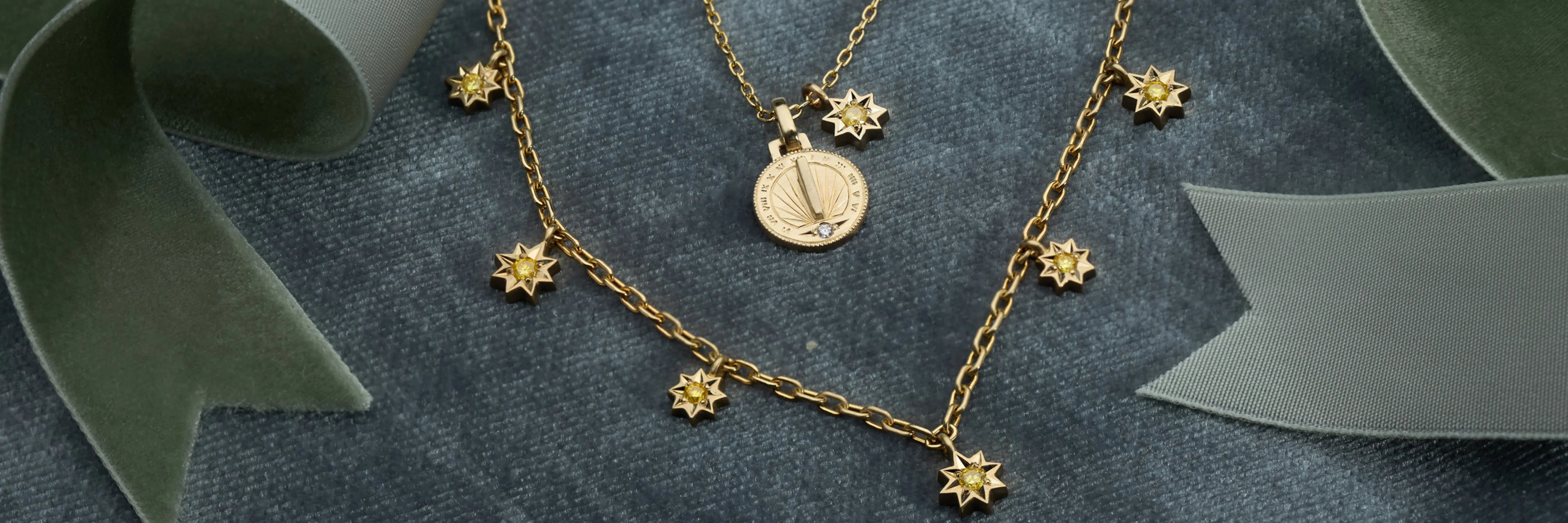Fairmined gold sundial pendant necklace and star charm chain on textured grey velvet background with green velvet ribbon