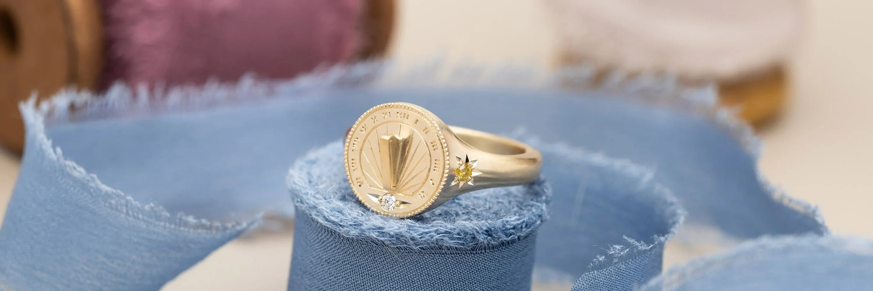 Close-up of handcrafted Fairmined gold sundial ring with diamond and yellow sapphire, soft natural light on blue fabric