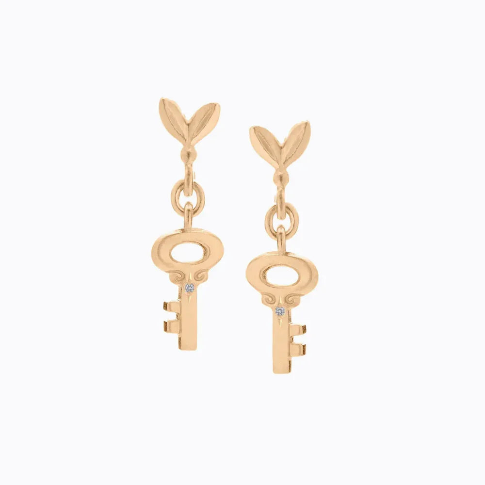 Hand-fabricated Fairmined gold key-shaped earrings with diamond accents on soft white background
