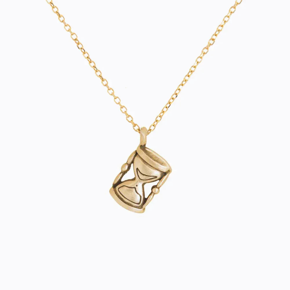 Handcrafted Fairmined gold hourglass pendant on delicate chain, warm natural light, minimalist white background