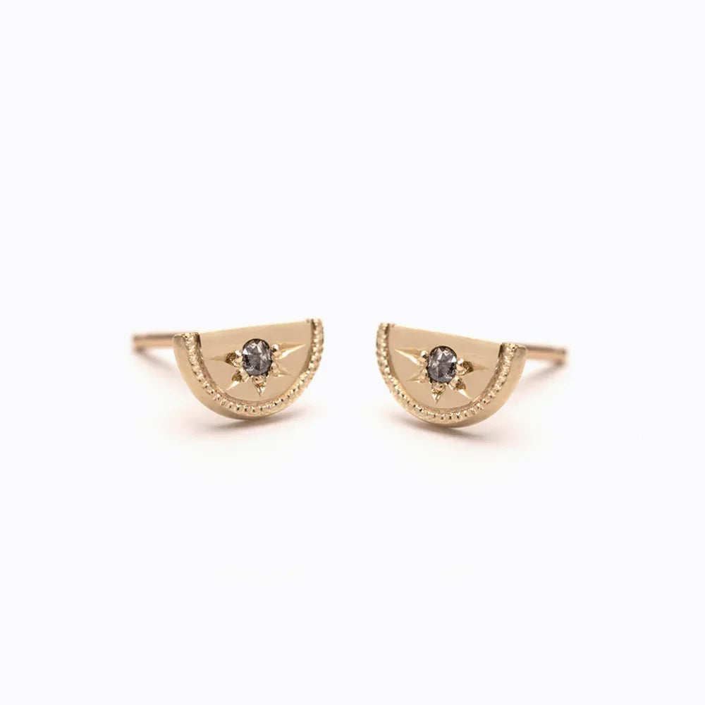 Close-up of handcrafted 14k gold half-moon stud earrings with central dark stone and milgrain edge on white background
