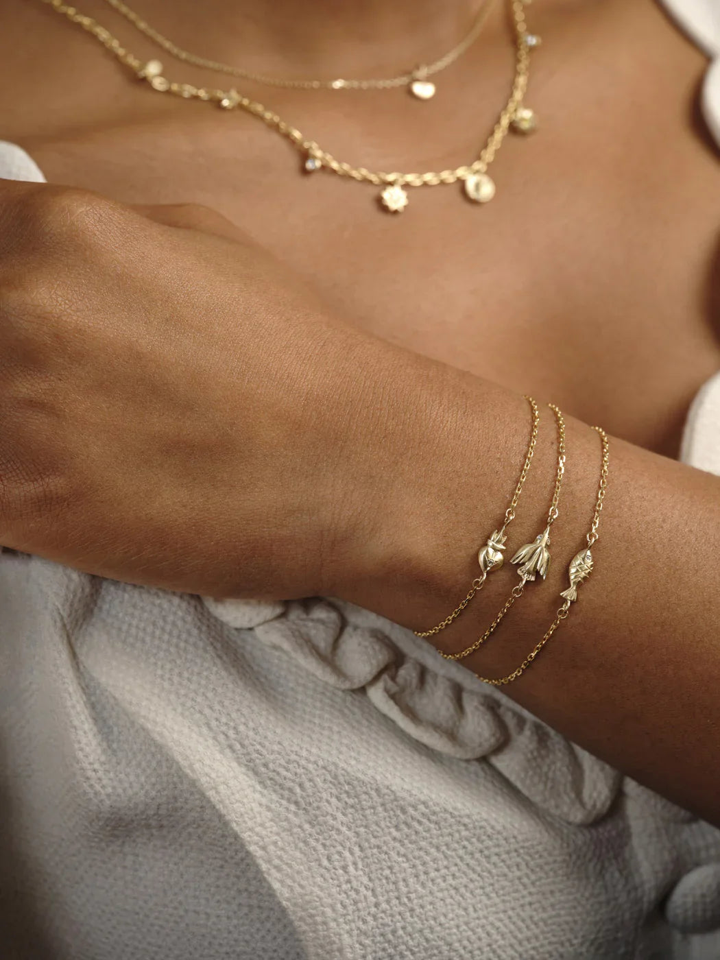 Close-up of hand-fabricated gold charm bracelets with heart, flower, and fish motifs, warm natural light