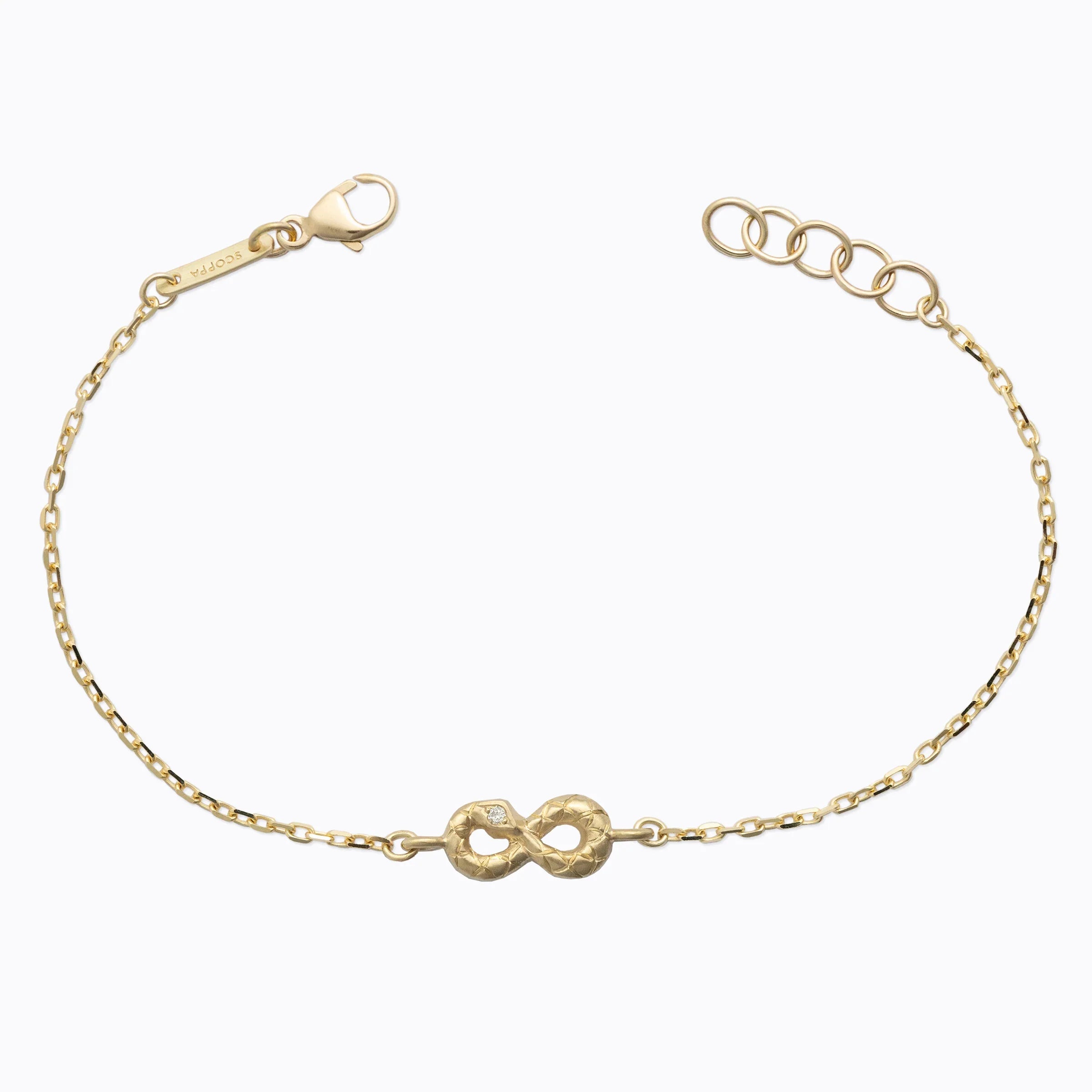 Delicate hand-fabricated gold infinity bracelet with subtle engraved texture and small diamond on white background