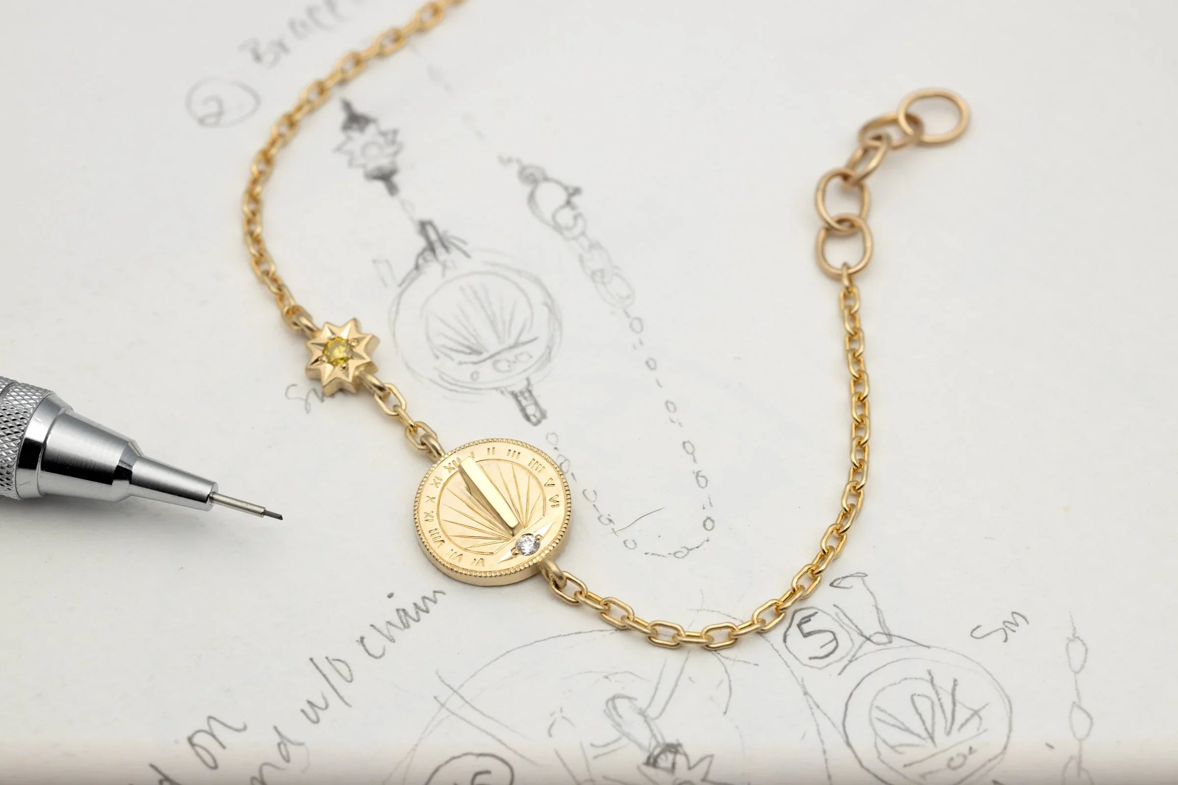 Handcrafted gold sundial bracelet with sun charm and diamond detail on sketch paper, soft natural light