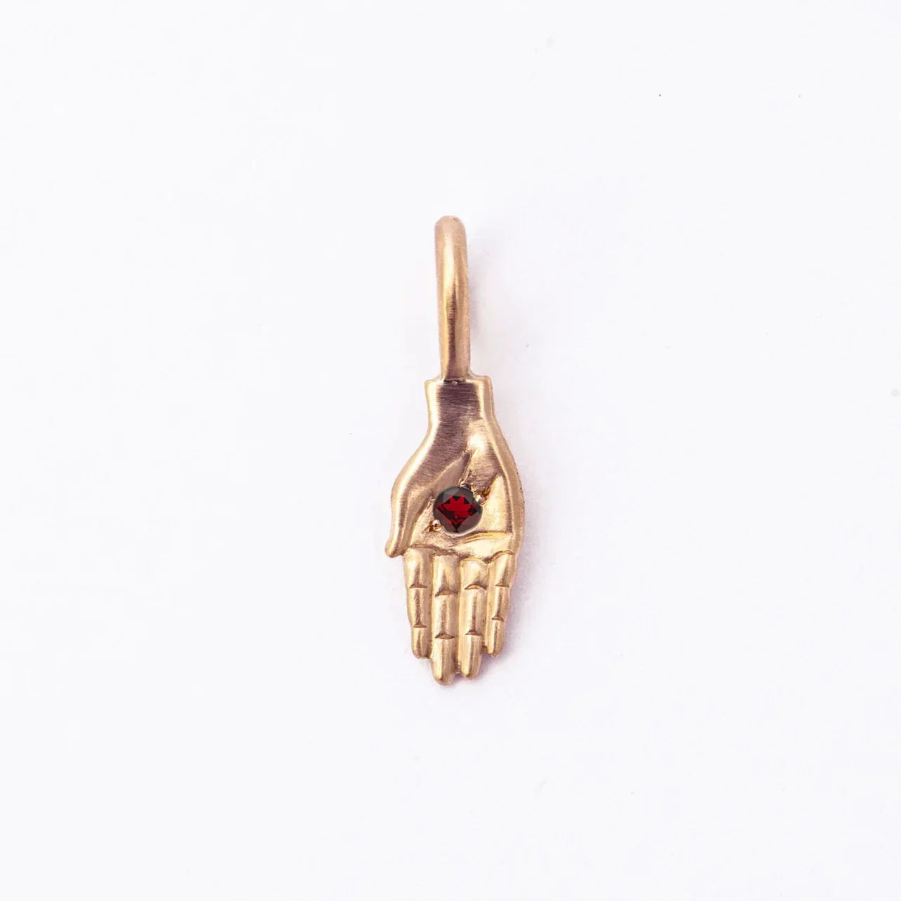 Handcrafted Fairmined gold pendant shaped as a detailed hand with a deep red gemstone, natural soft lighting