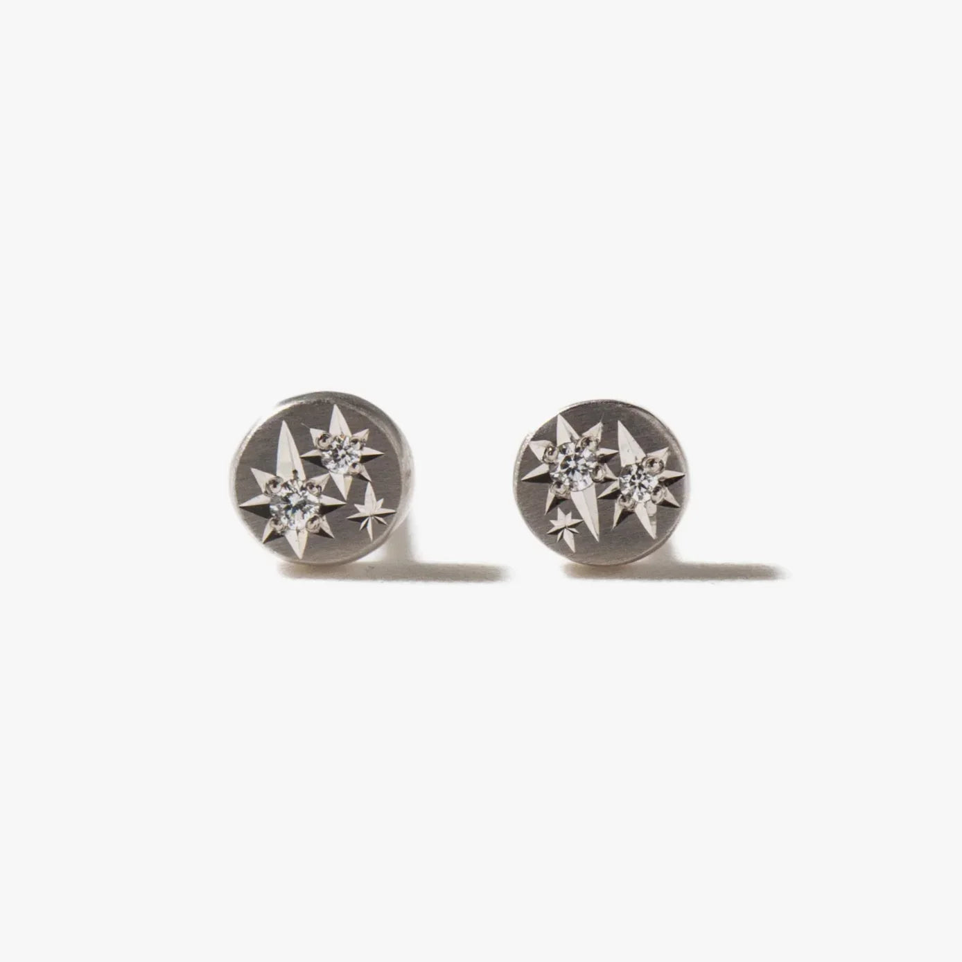 Close-up of platinum cosmic diamond stud earrings with star motifs, soft natural lighting on white background