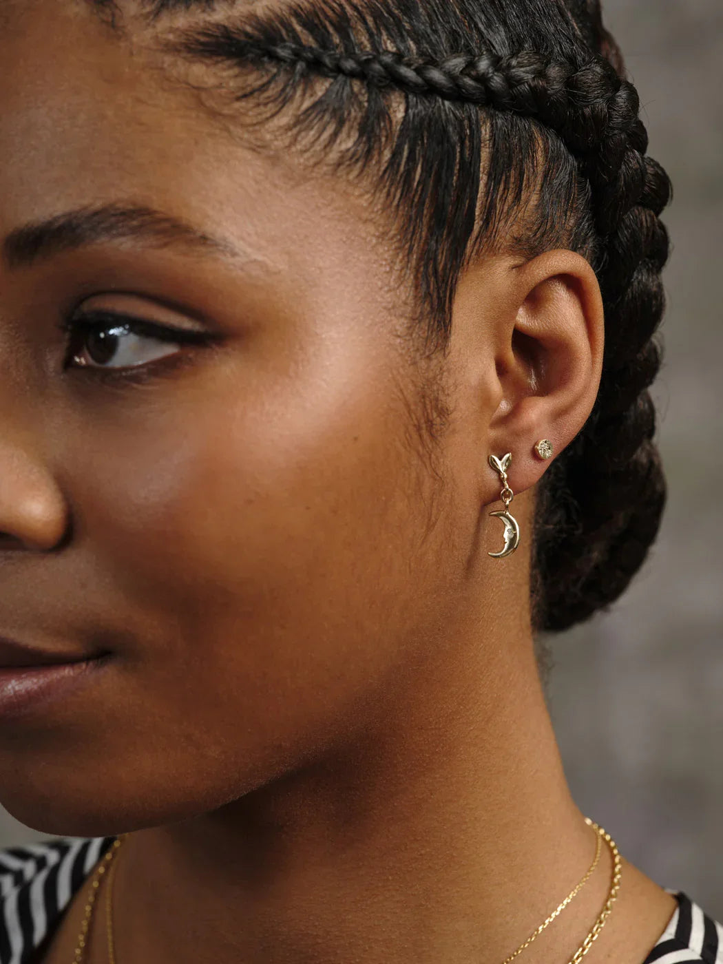 Close-up of woman wearing hand-engraved gold moon phase drop earring and small gold stud, warm natural light