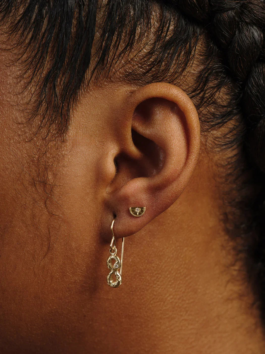 Close-up of ear wearing handcrafted gold earrings with intricate design and warm natural light