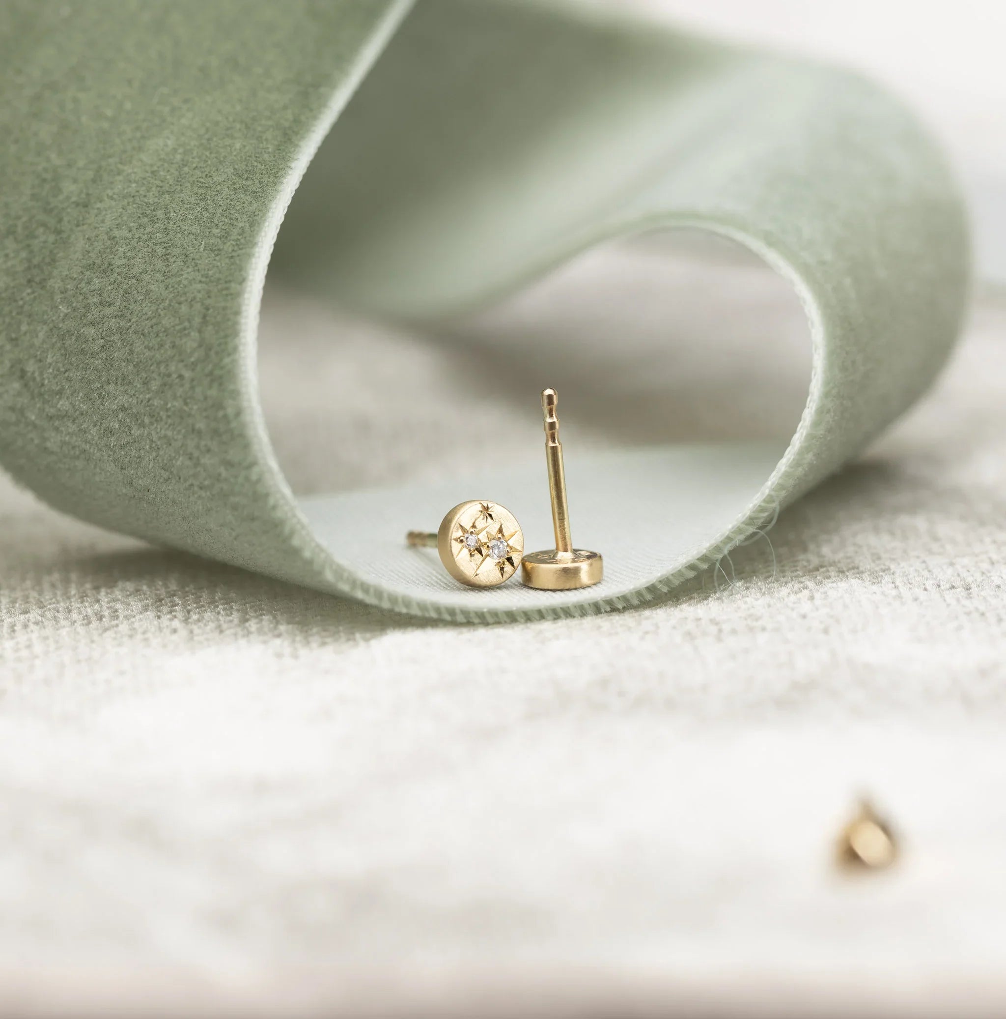 Close-up of handcrafted gold stud earrings with star engraving and diamond detail on soft beige fabric