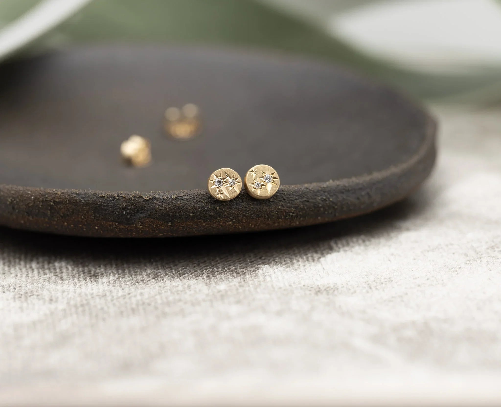 Close-up of handcrafted Fairmined gold starburst stud earrings with diamonds on rustic dark plate and linen