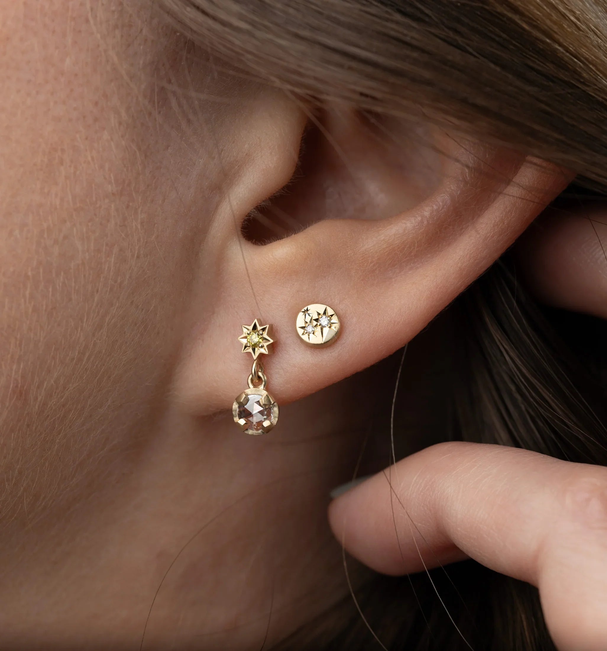 Close-up of hand-fabricated gold star and gemstone earrings on ear, natural warm lighting