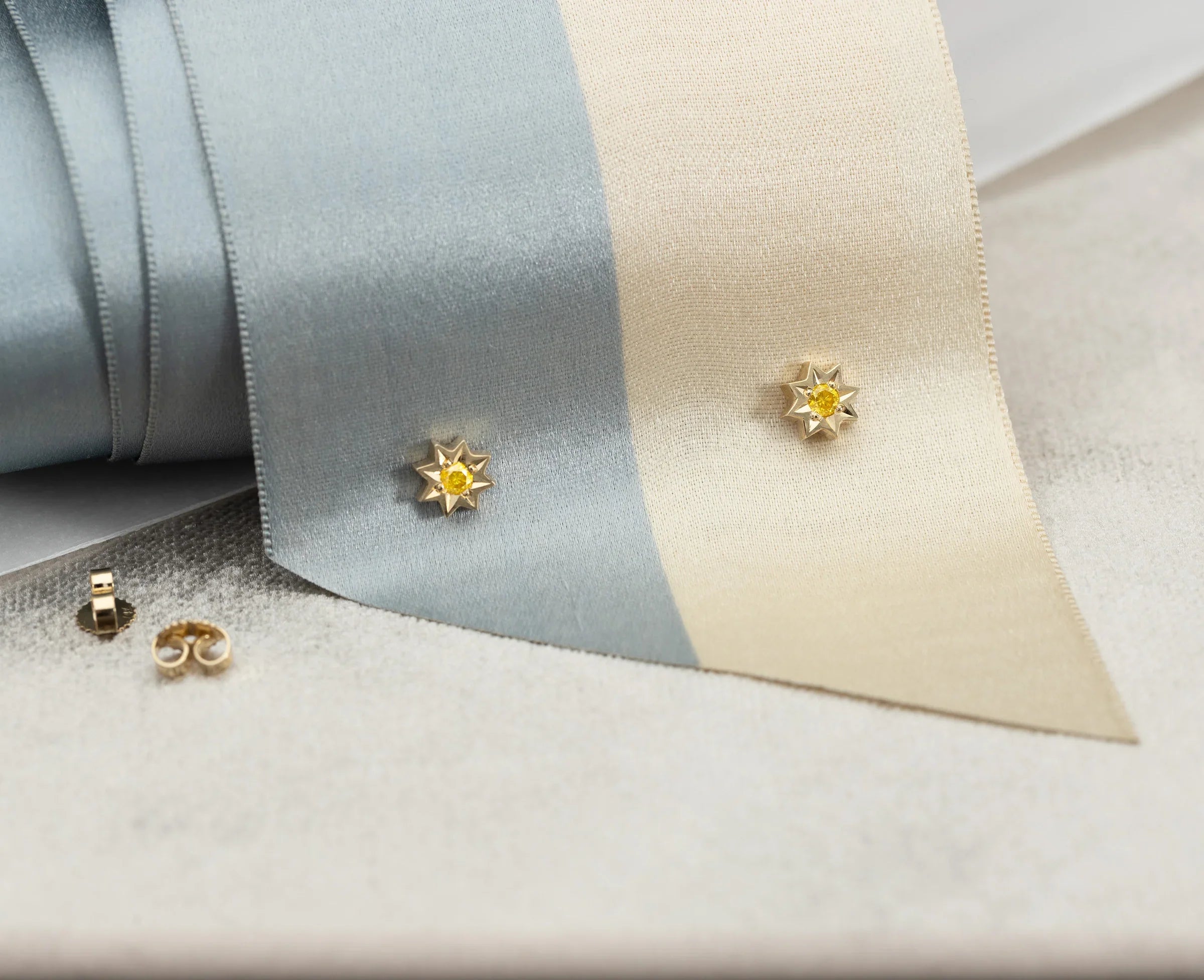 Close-up of handcrafted gold star-shaped earrings with yellow gemstone centers on soft beige and gray fabric