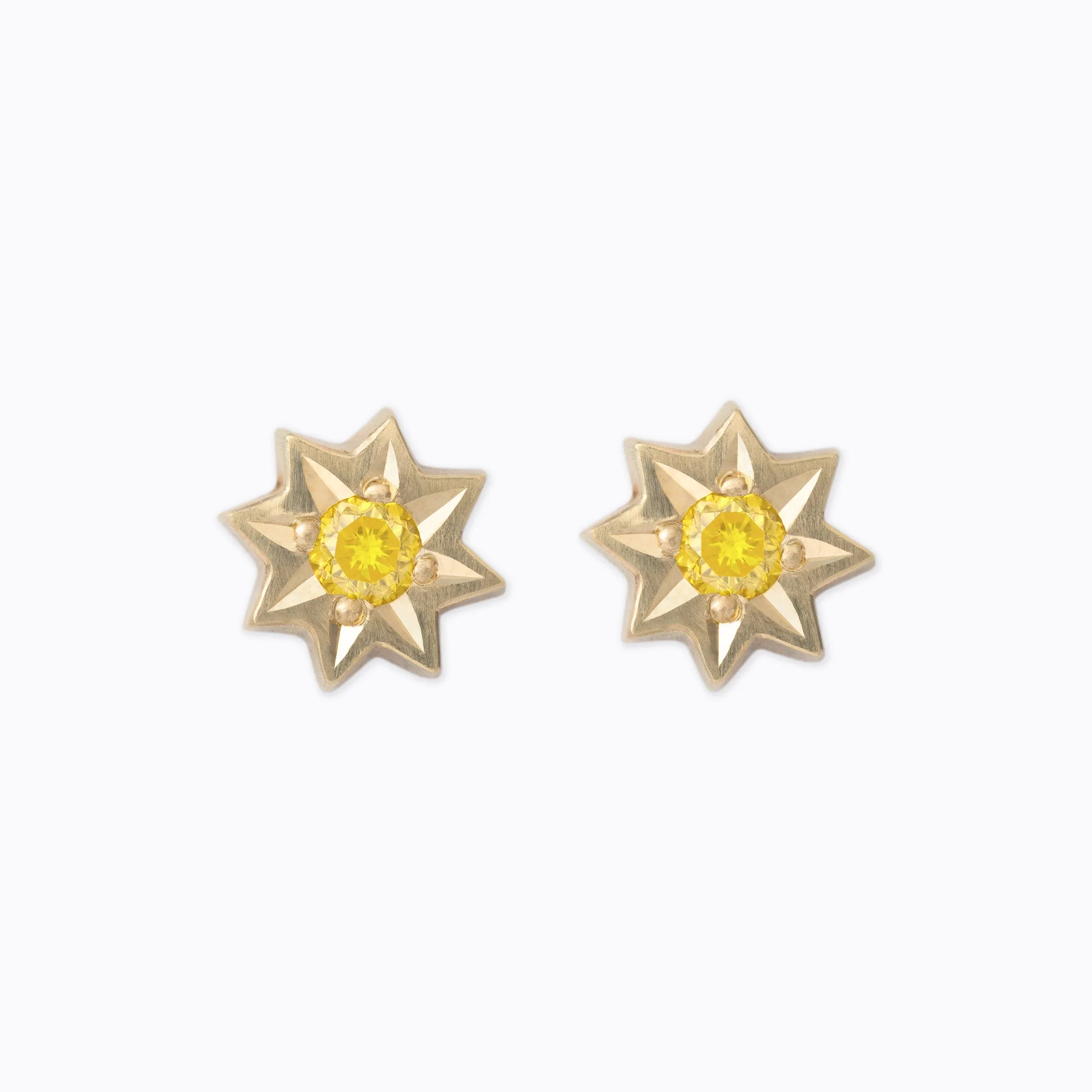 Pair of eight-point star-shaped gold stud earrings with faceted yellow center stones on white background