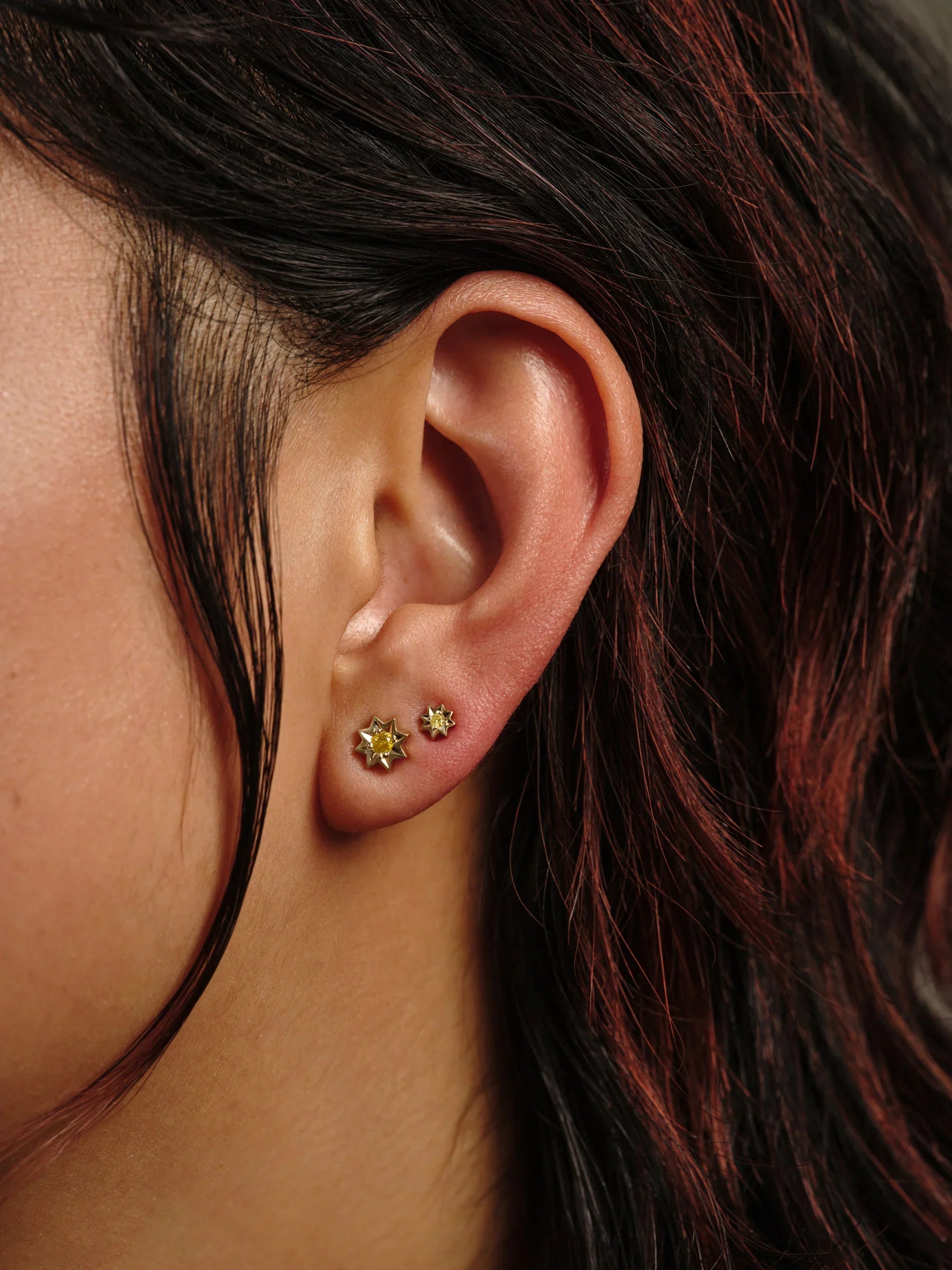 Close-up of ear wearing handcrafted Fairmined gold sunburst stud earrings with warm golden hour light