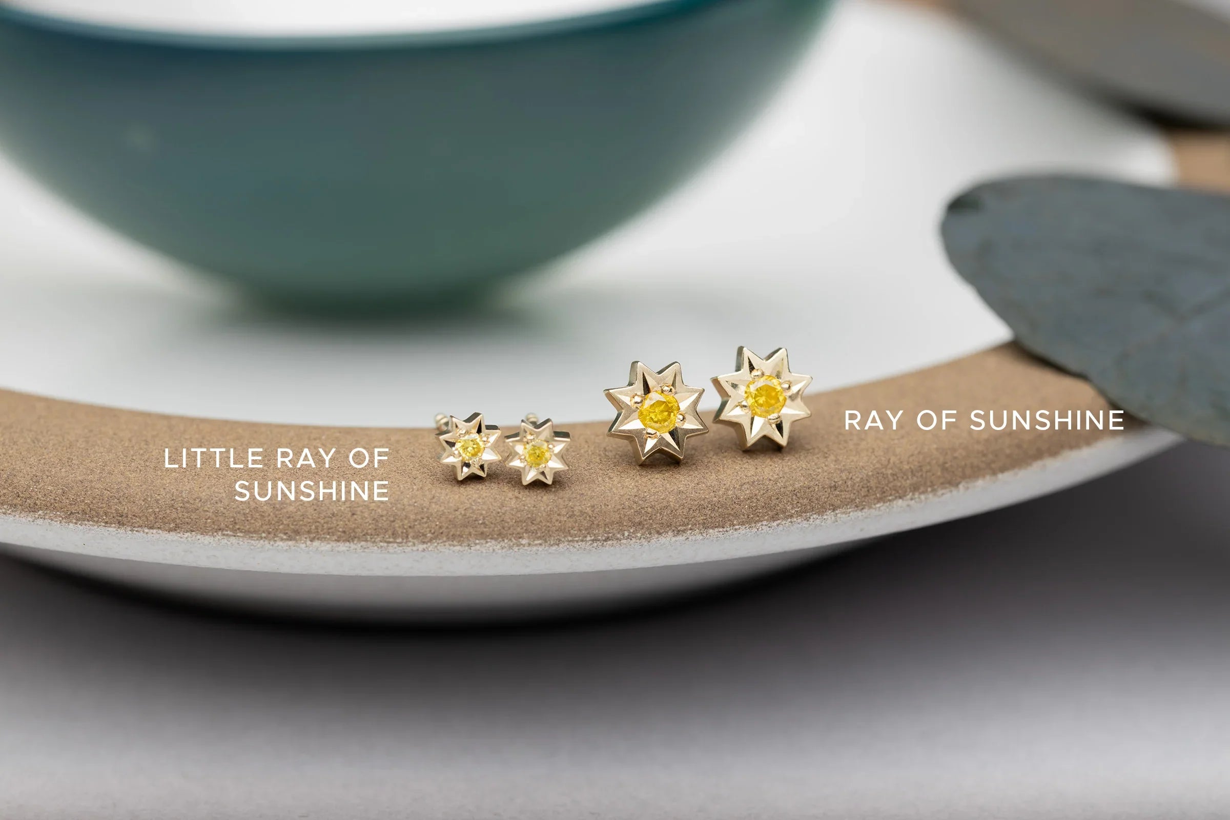 Close-up of gold star-shaped earrings with yellow gemstones on textured ceramic surface, soft natural light