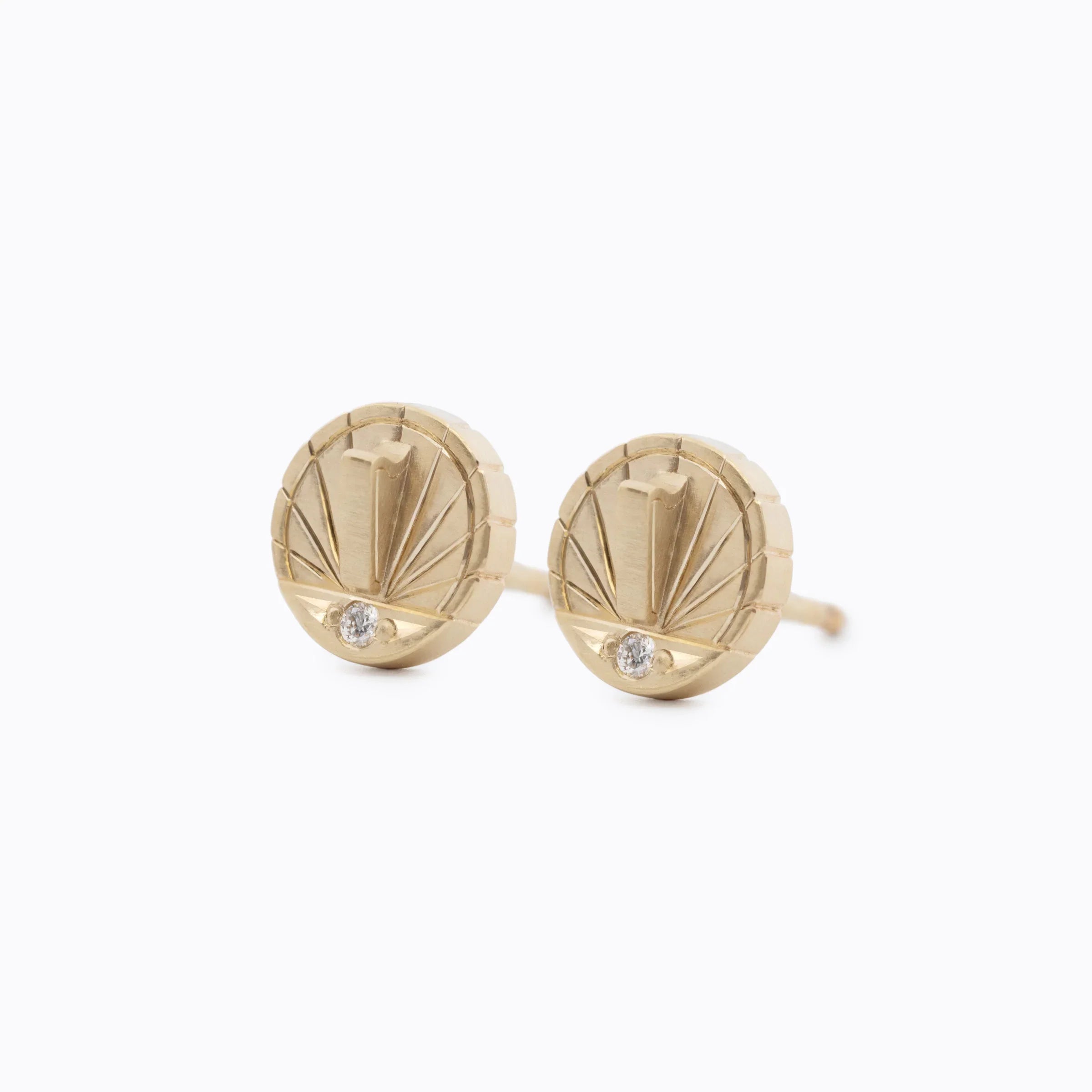 Pair of handcrafted Fairmined gold stud earrings with sunburst design and small diamond detail on white background