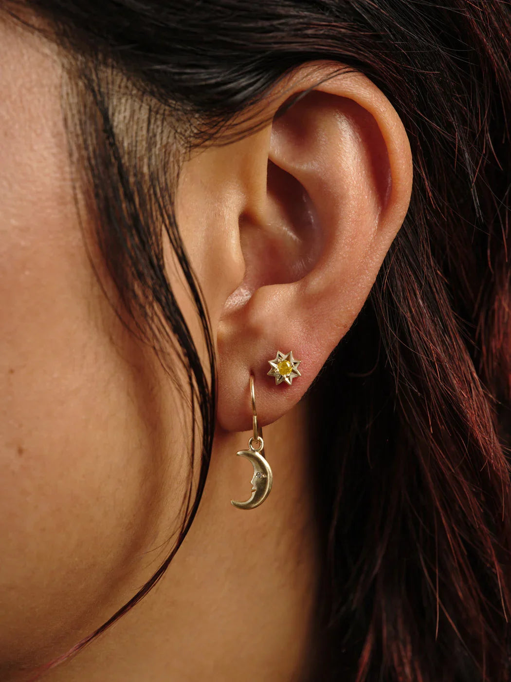 Close-up of ear wearing delicate gold moon phase earrings with crescent moon charm and star stud