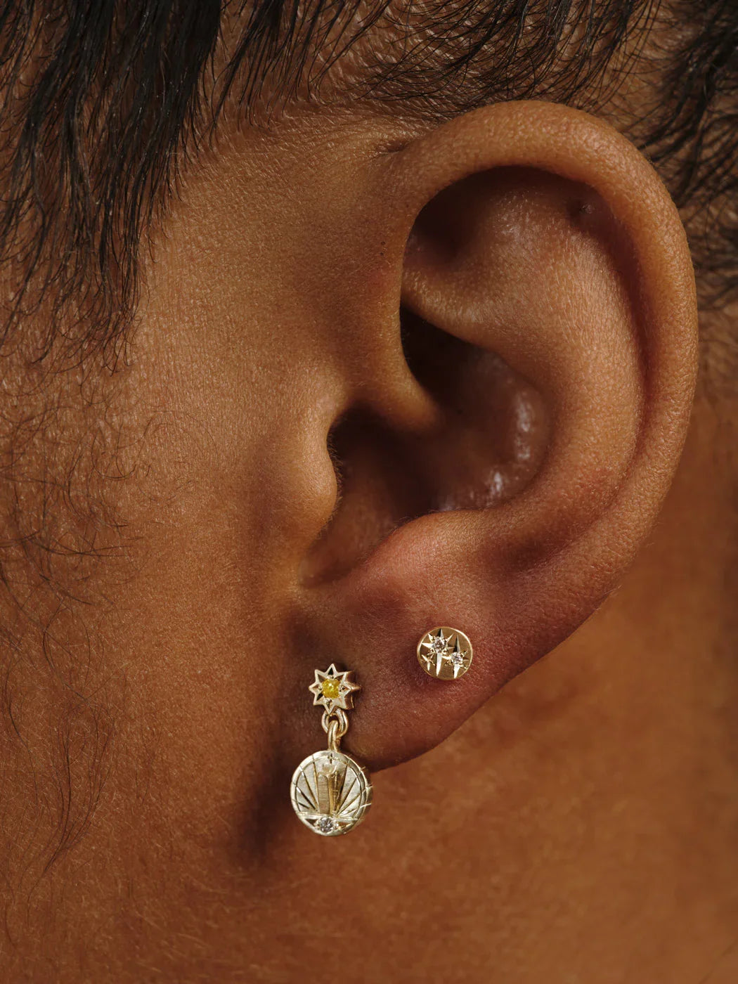 Close-up of ear wearing handcrafted Fairmined gold celestial earrings with star motifs and warm natural light