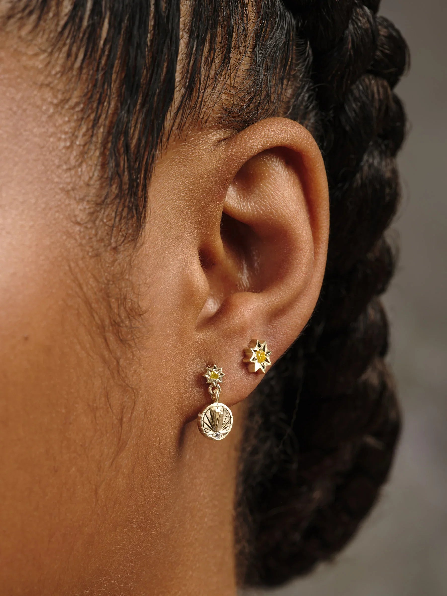 Close-up of ear wearing handcrafted Fairmined gold yellow gemstone star stud and matching sun pendant earring in soft natural light