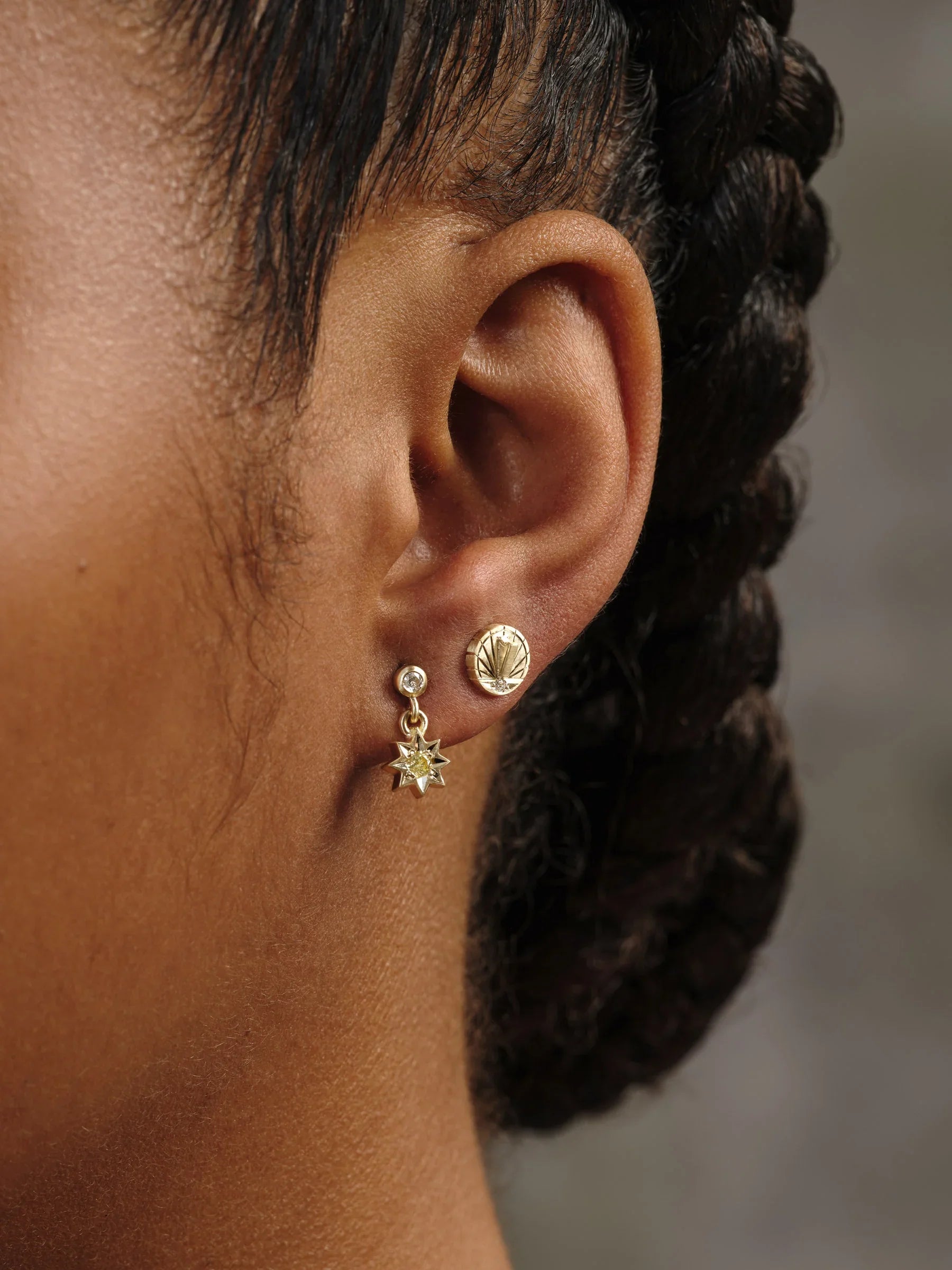 Close-up of ear wearing handcrafted gold sunburst stud and star drop earrings with diamond accents