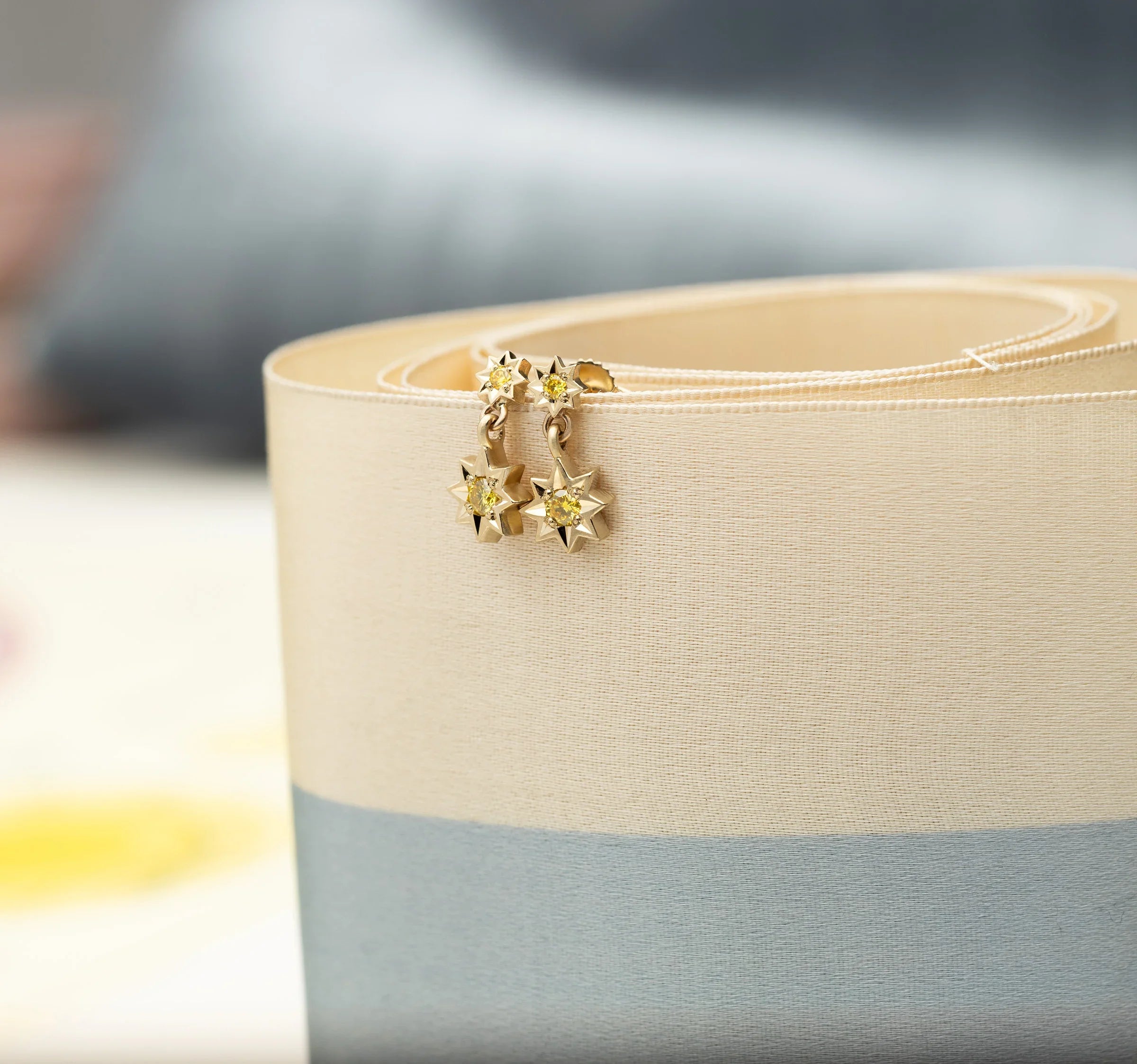 Hand-fabricated Fairmined gold star-shaped drop earrings with yellow stones on beige linen