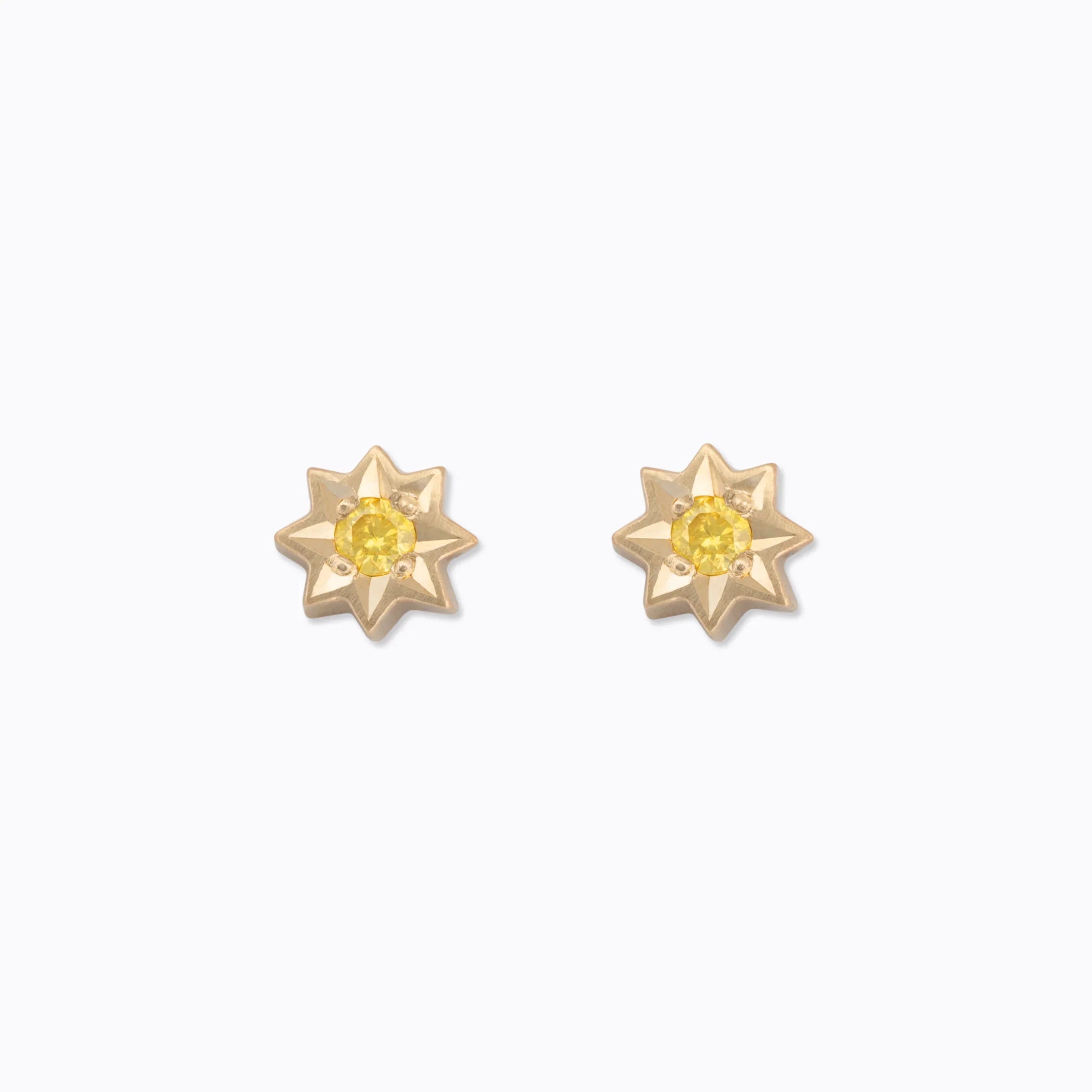 Pair of gold star-shaped stud earrings with yellow gemstone centers on white background