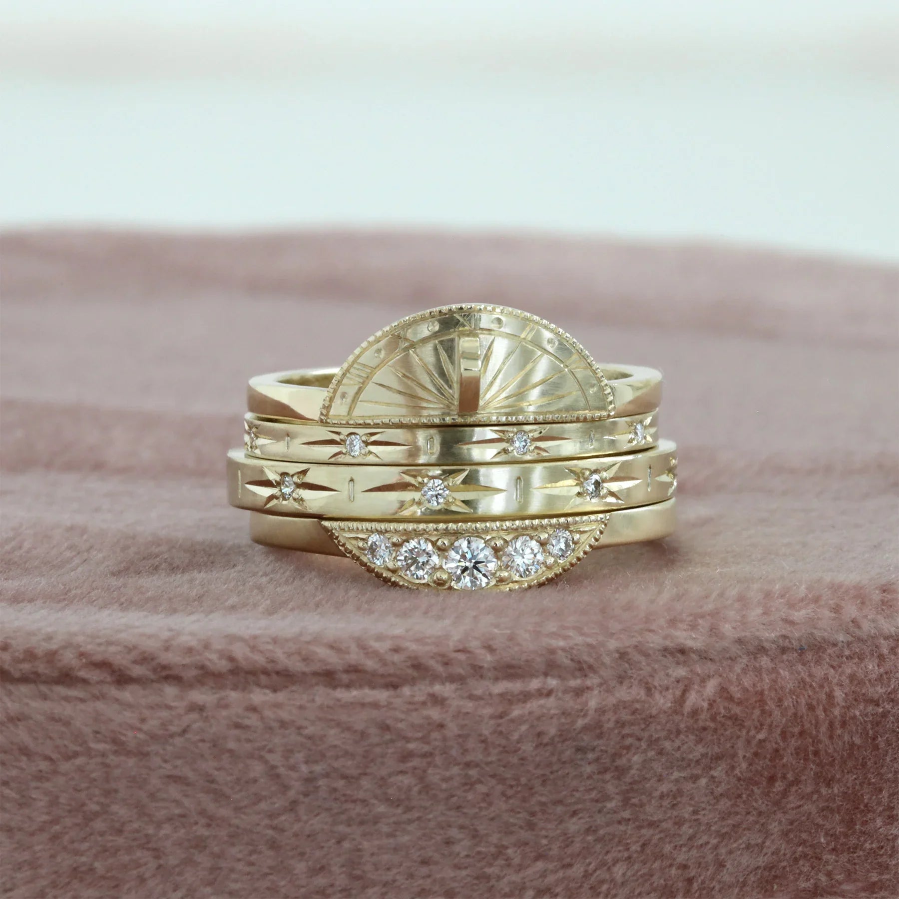 Stacked handcrafted Fairmined gold sundial rings with diamonds on soft textured surface in warm natural light