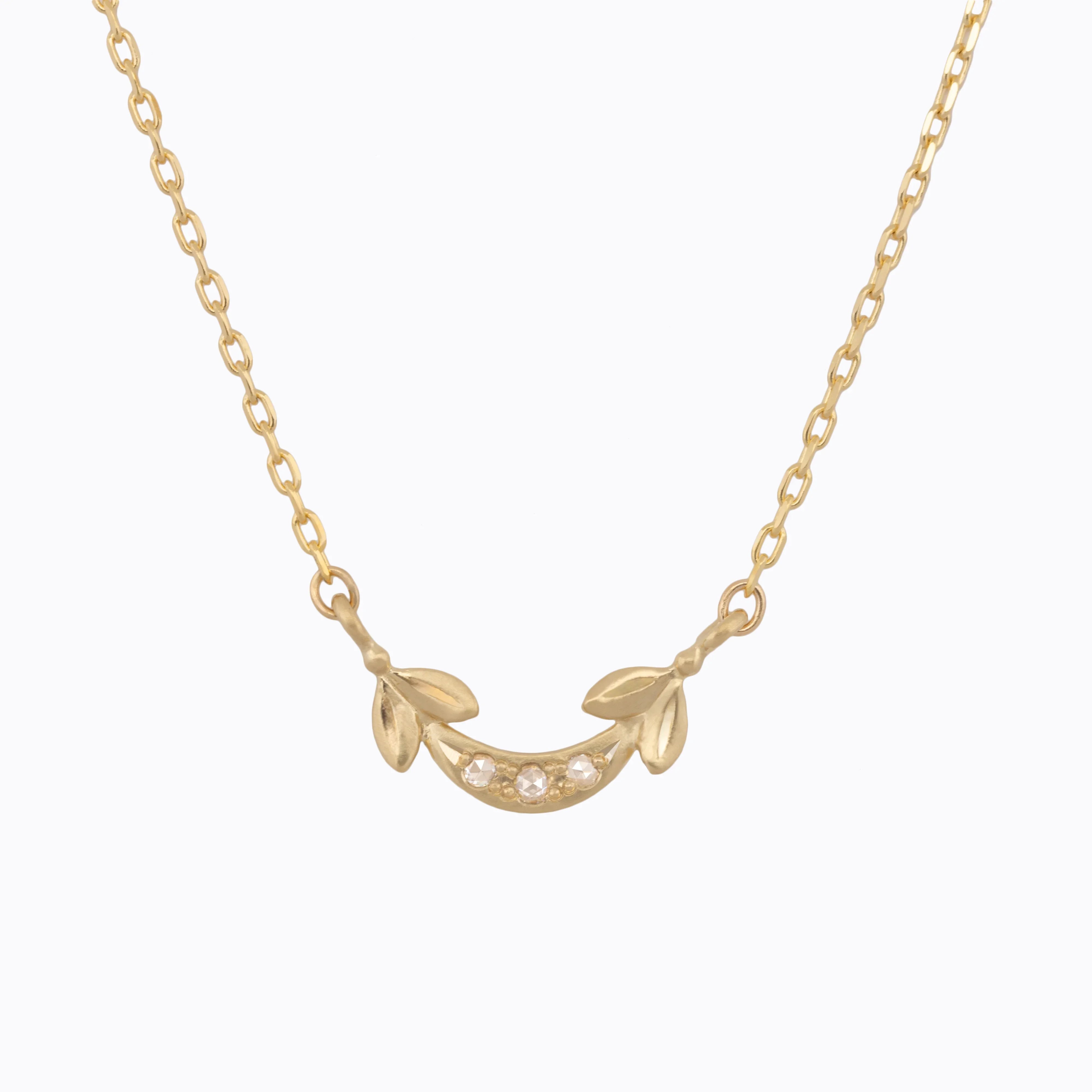 Delicate Fairmined gold necklace with leaf details and three small gem accents on soft white background