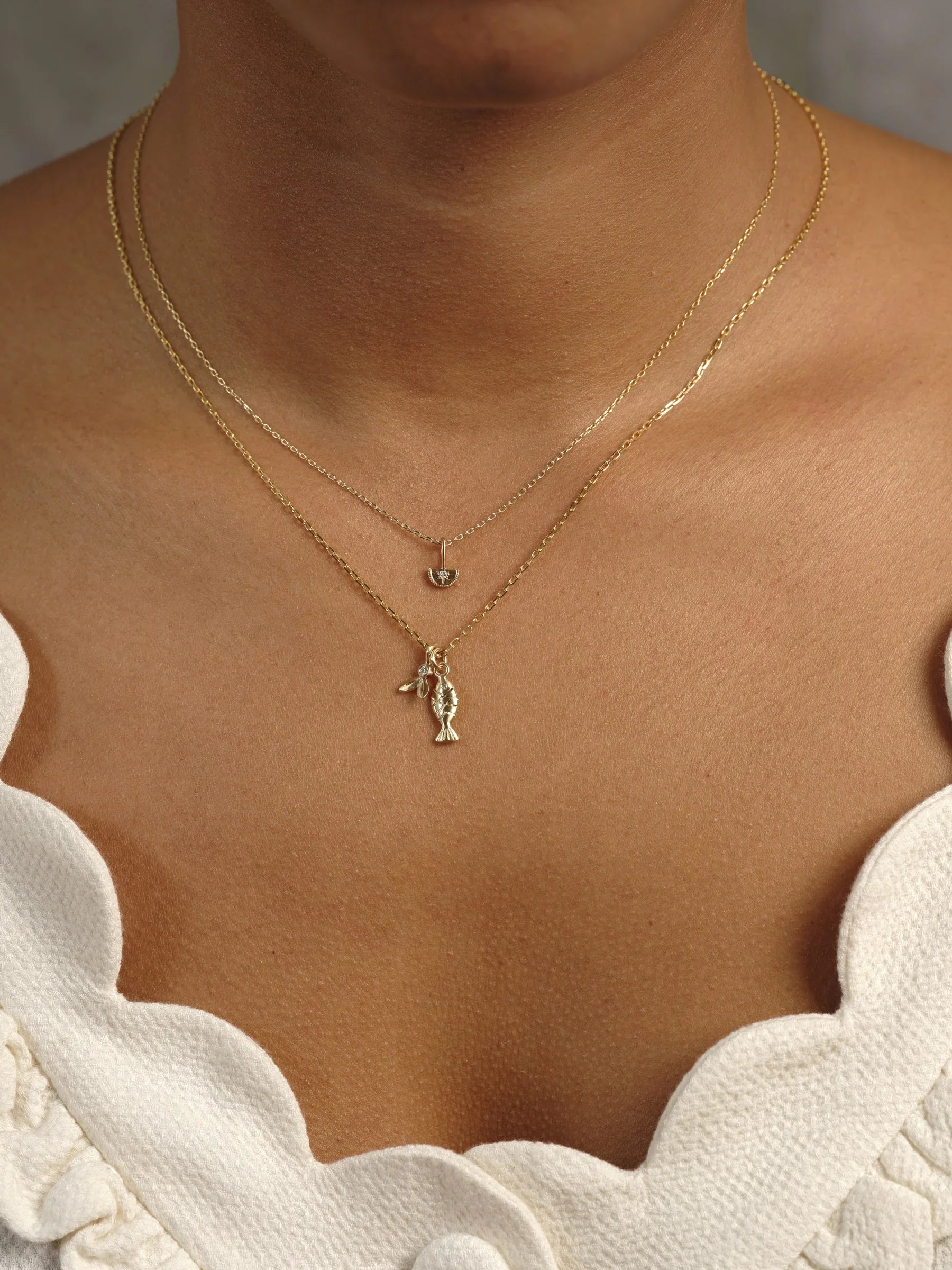 Close-up of layered Fairmined gold necklaces with fish and charm pendants on warm skin in soft natural light