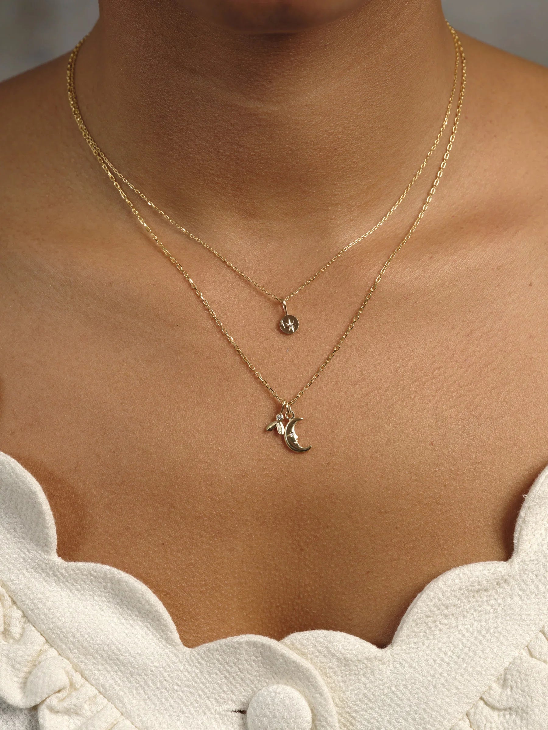 Close-up of layered 18k gold necklaces with star and crescent moon pendants on natural skin and white textured top