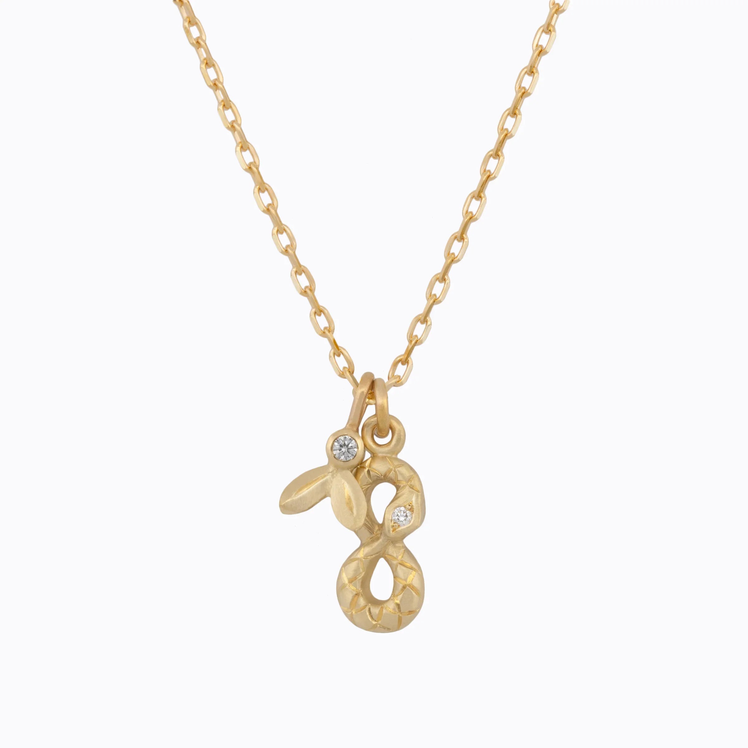 Hand-fabricated gold snake pendant with diamond accents on delicate gold chain, minimalist white background