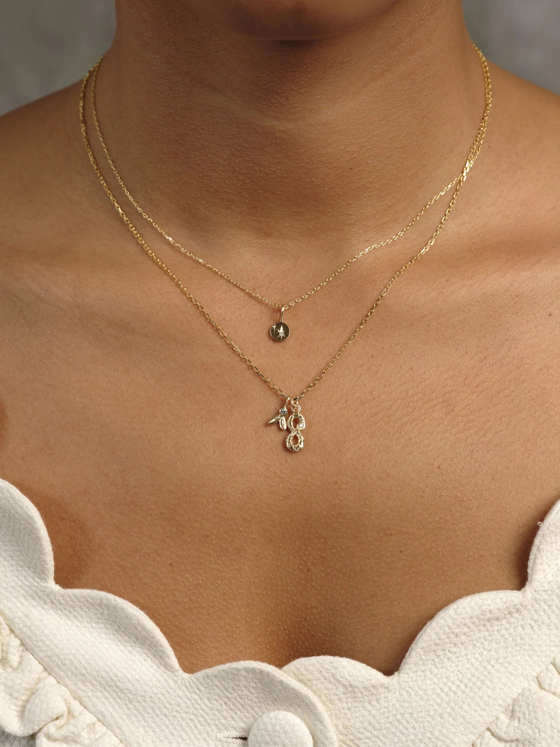 Close-up of layered delicate 14k gold necklaces with star and textured pendants on natural skin, warm light