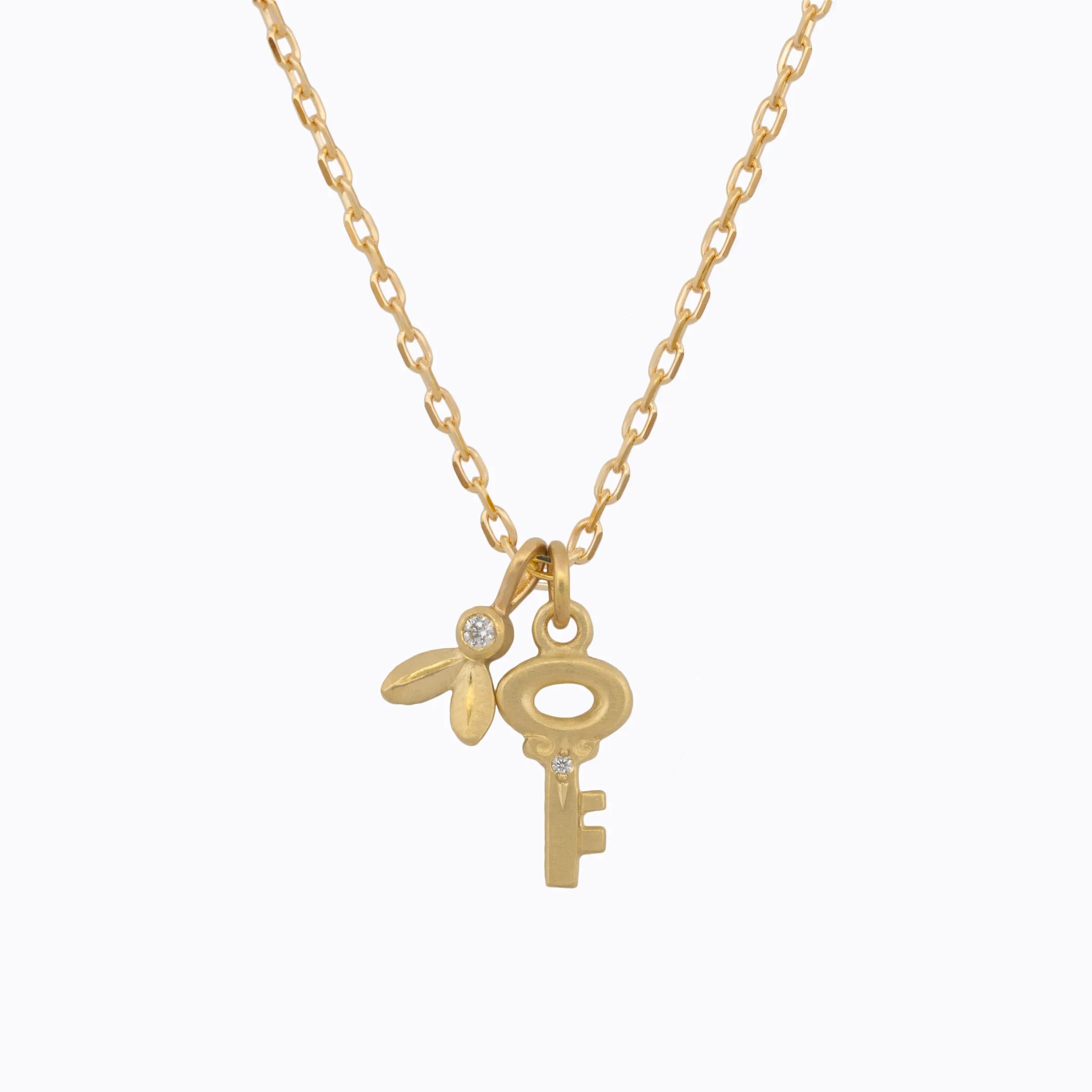 Delicate gold key and leaf pendants with small diamonds on fine gold chain, minimalist white background