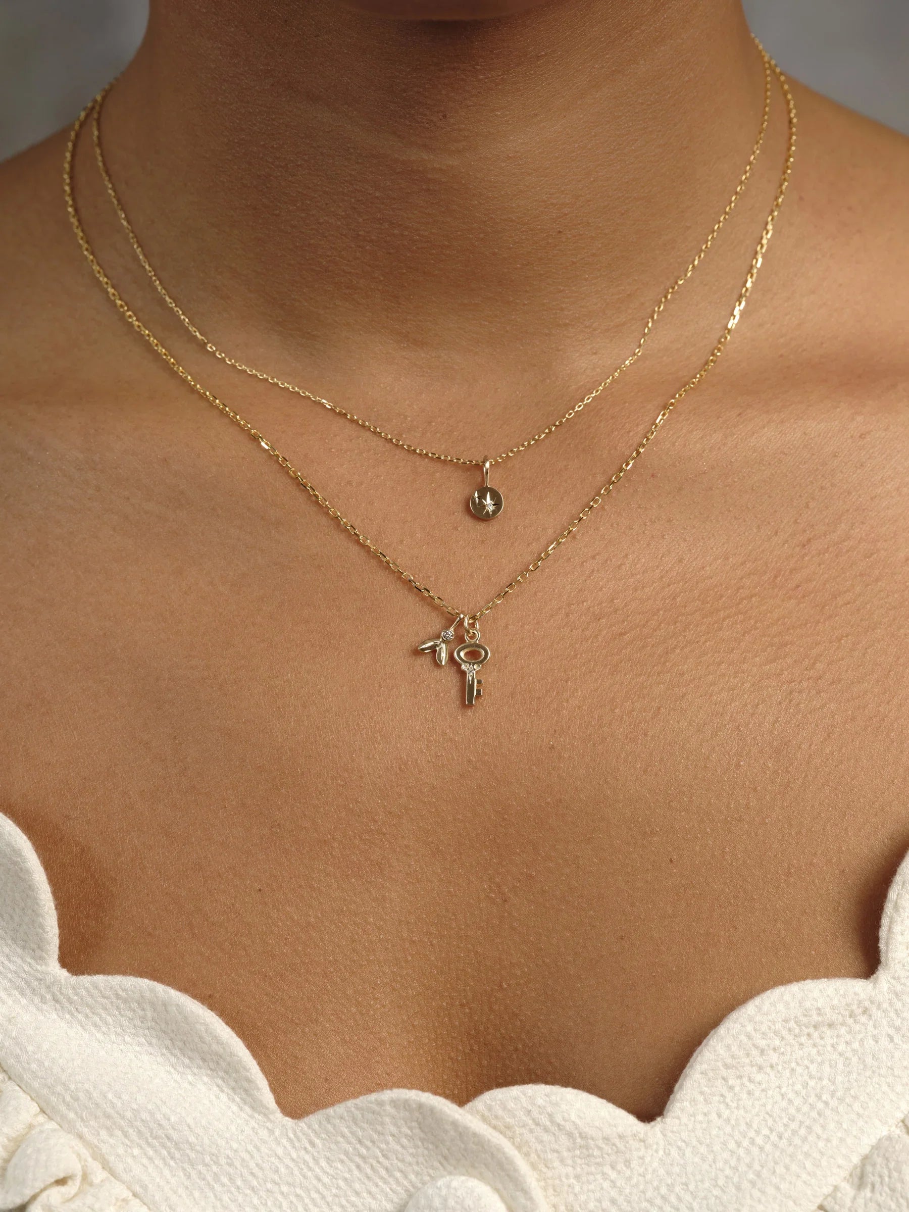 Golden hour close-up of layered delicate gold necklaces with star and key pendants on warm skin