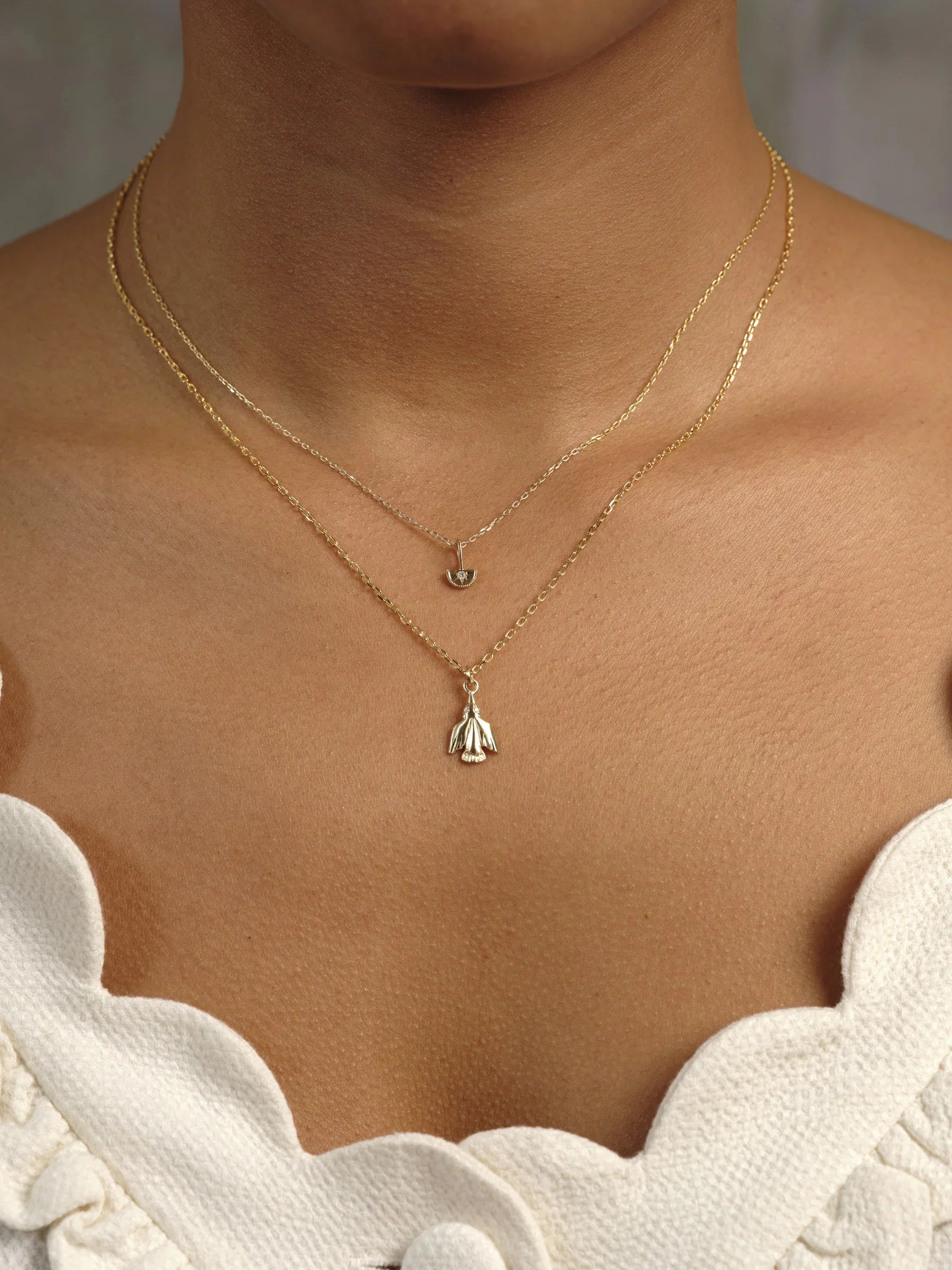 Close-up of layered delicate gold necklaces with botanical pendants on natural skin, soft neutral background