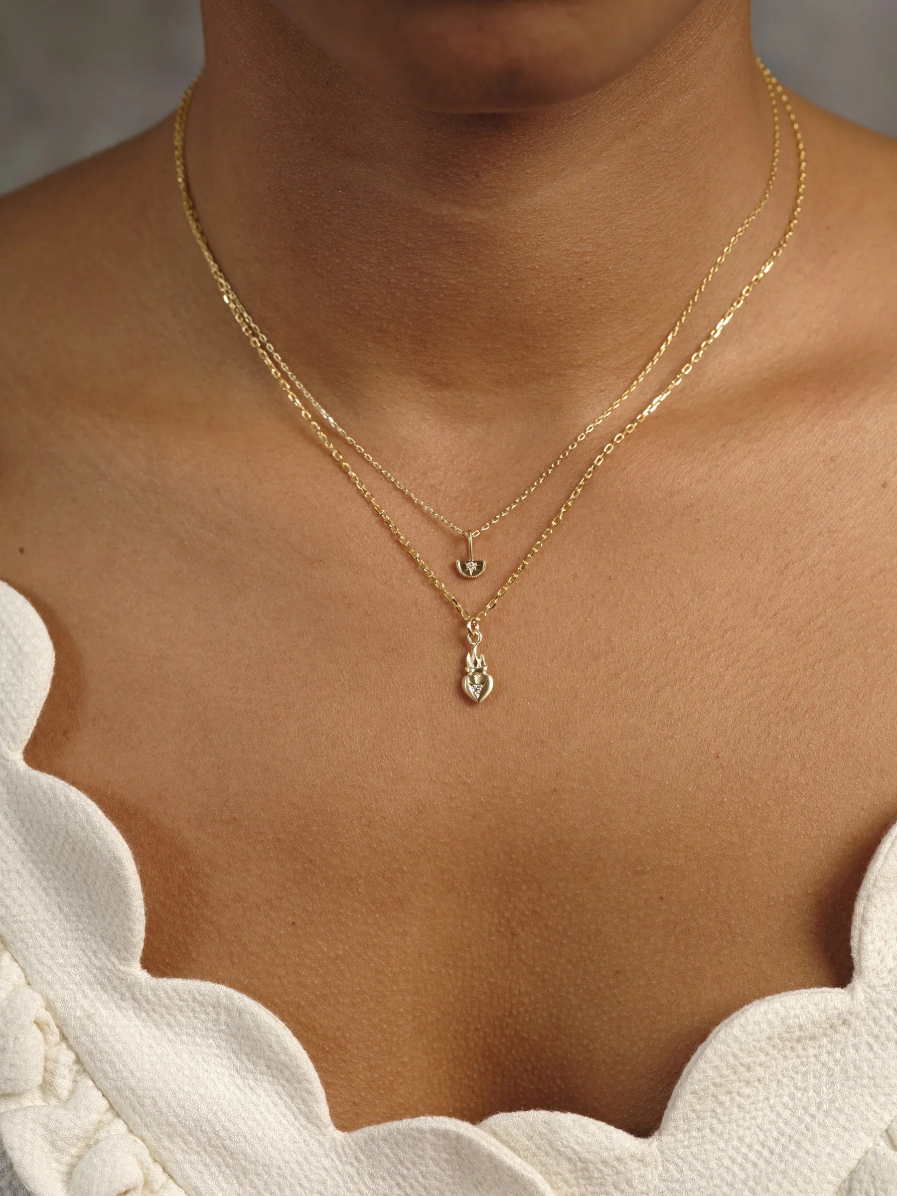 Two layered delicate gold necklaces with heart pendants on neckline, warm natural light on skin