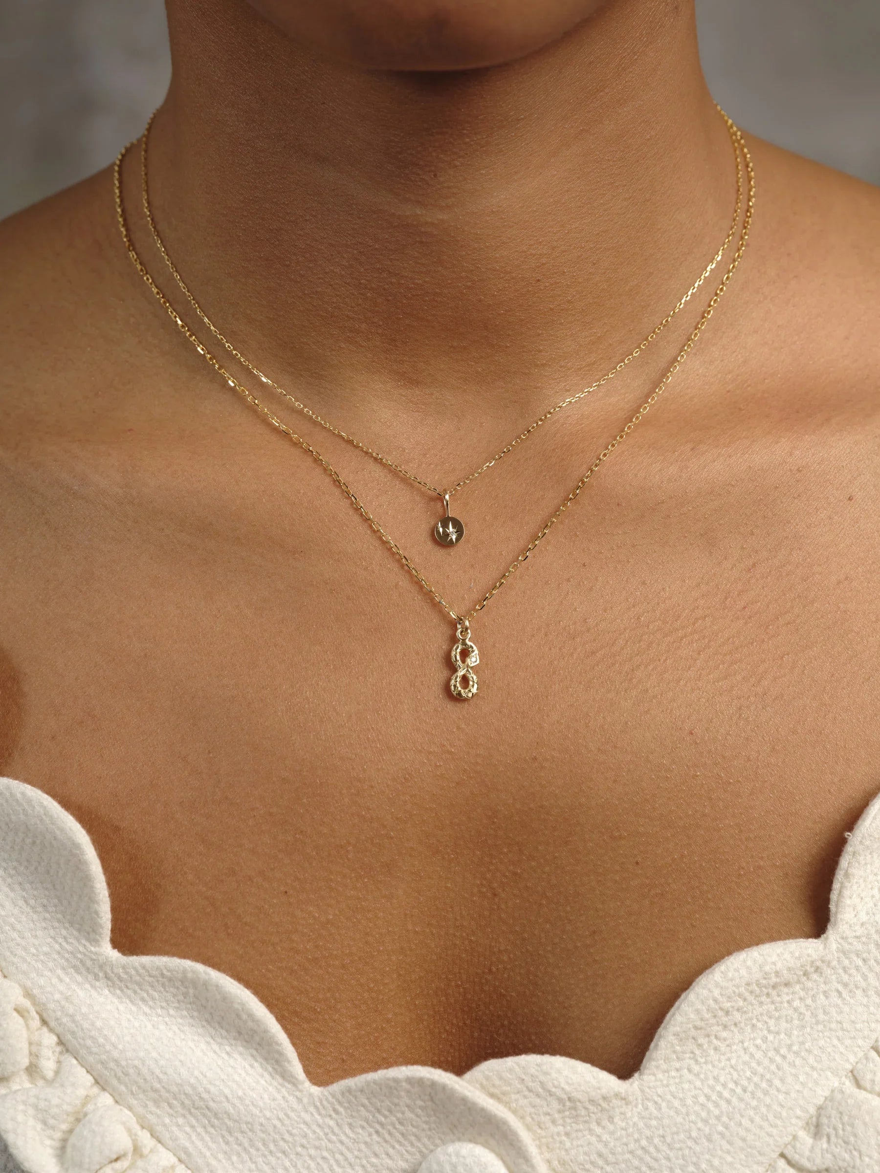Close-up of layered hand-fabricated gold necklaces on collarbone, warm natural light on smooth skin and white scalloped top