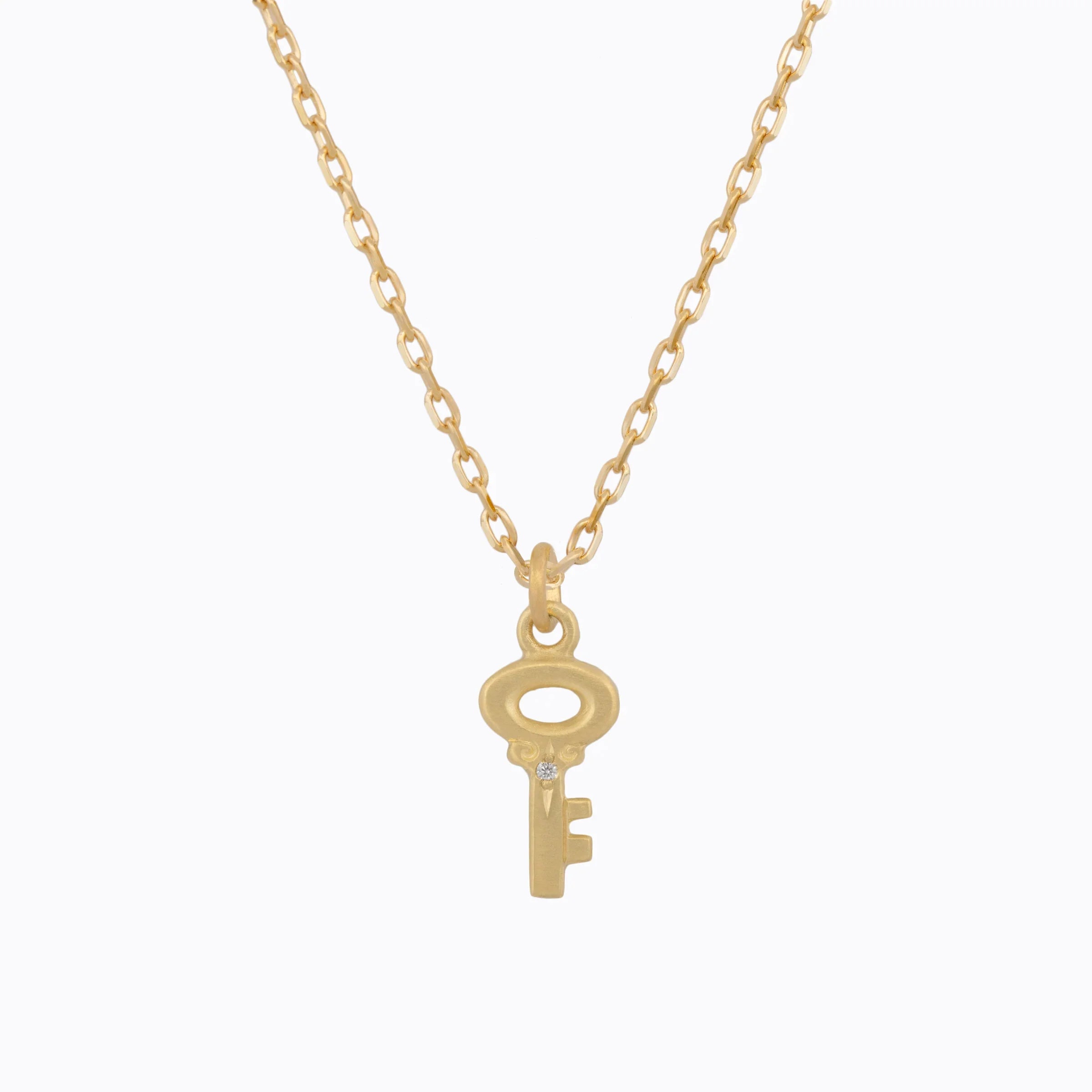 Delicate gold key pendant necklace with small diamond accent on simple chain, white background