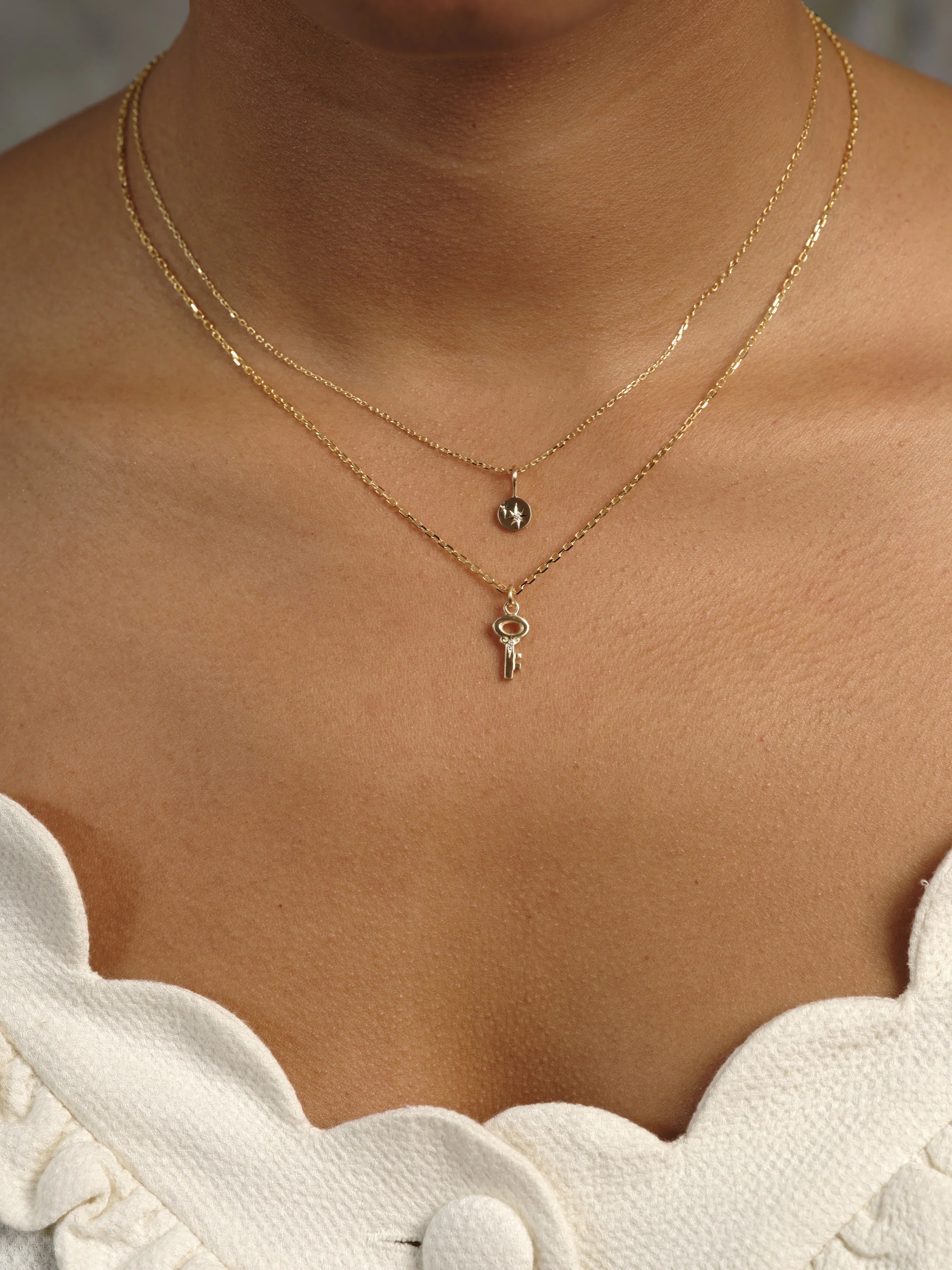 Close-up of layered delicate Fairmined gold necklaces with star and key pendants on warm skin, soft natural light