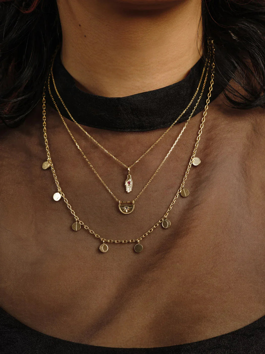 Layered Fairmined gold necklaces with hand-engraved pendants worn against dark skin and black top