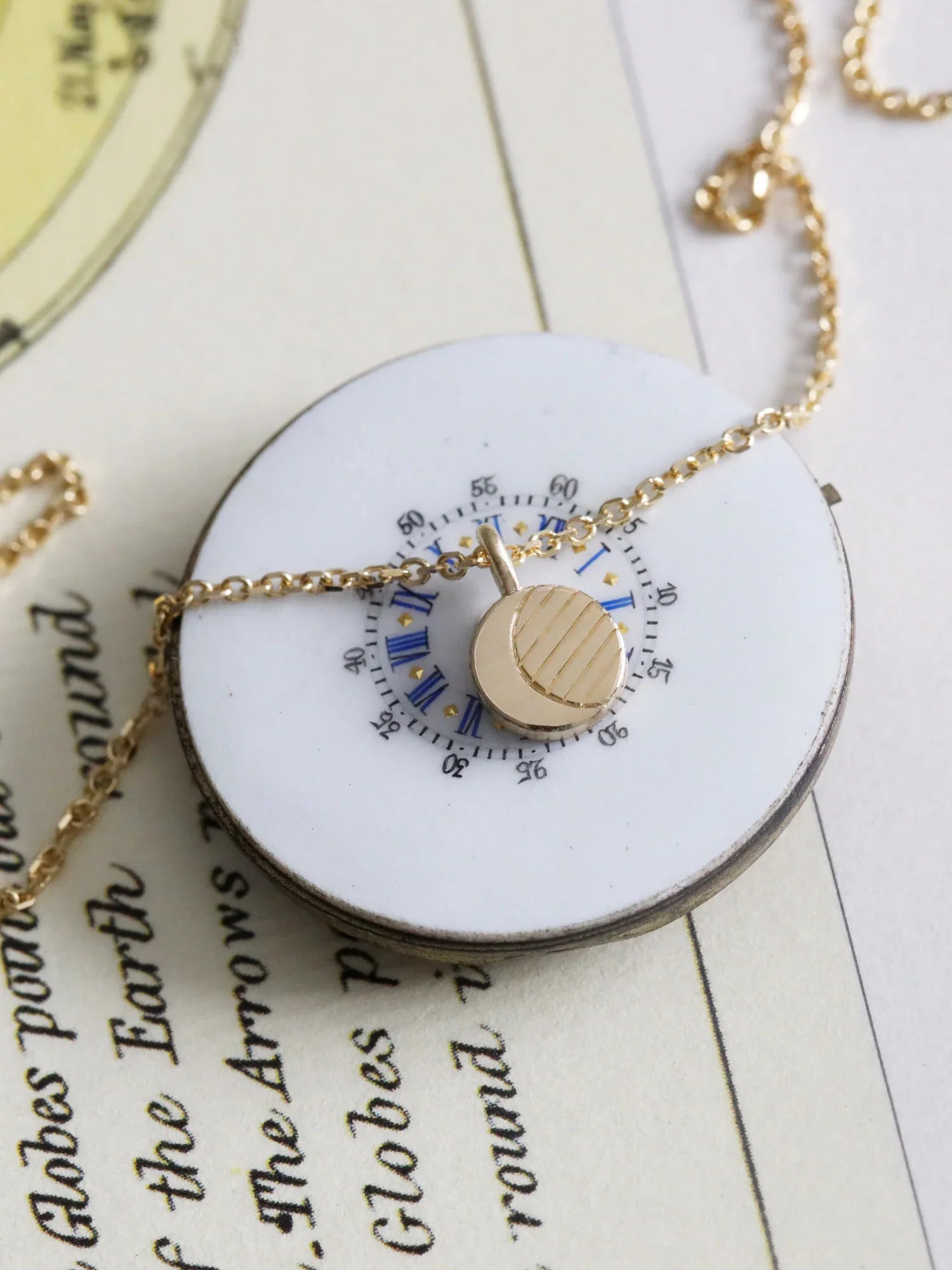 Delicate gold moon phase pendant on chain, resting on vintage celestial map background with natural light