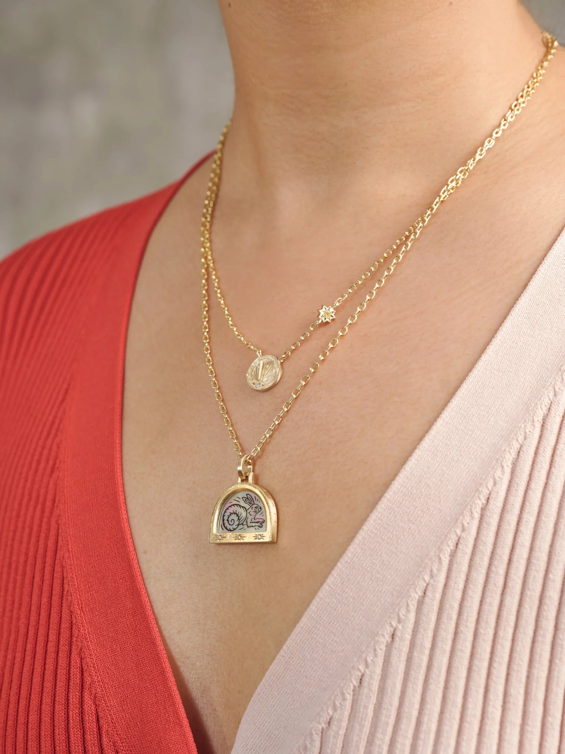Close-up of layered Fairmined gold necklaces with engraved oval pendant and illustrated charm, warm natural light
