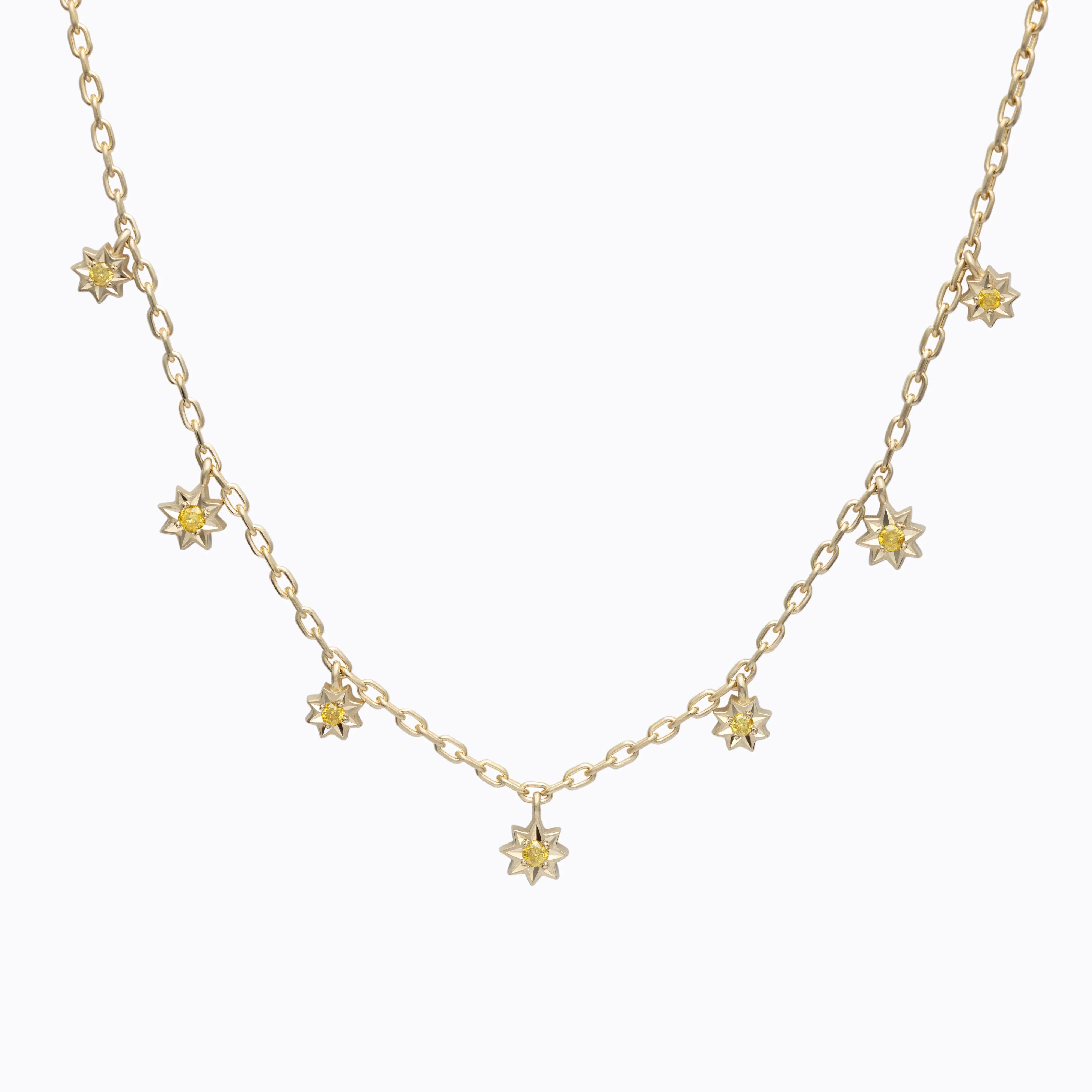 Delicate gold chain necklace with seven eight-point star charms, each set with yellow gemstones, on white background